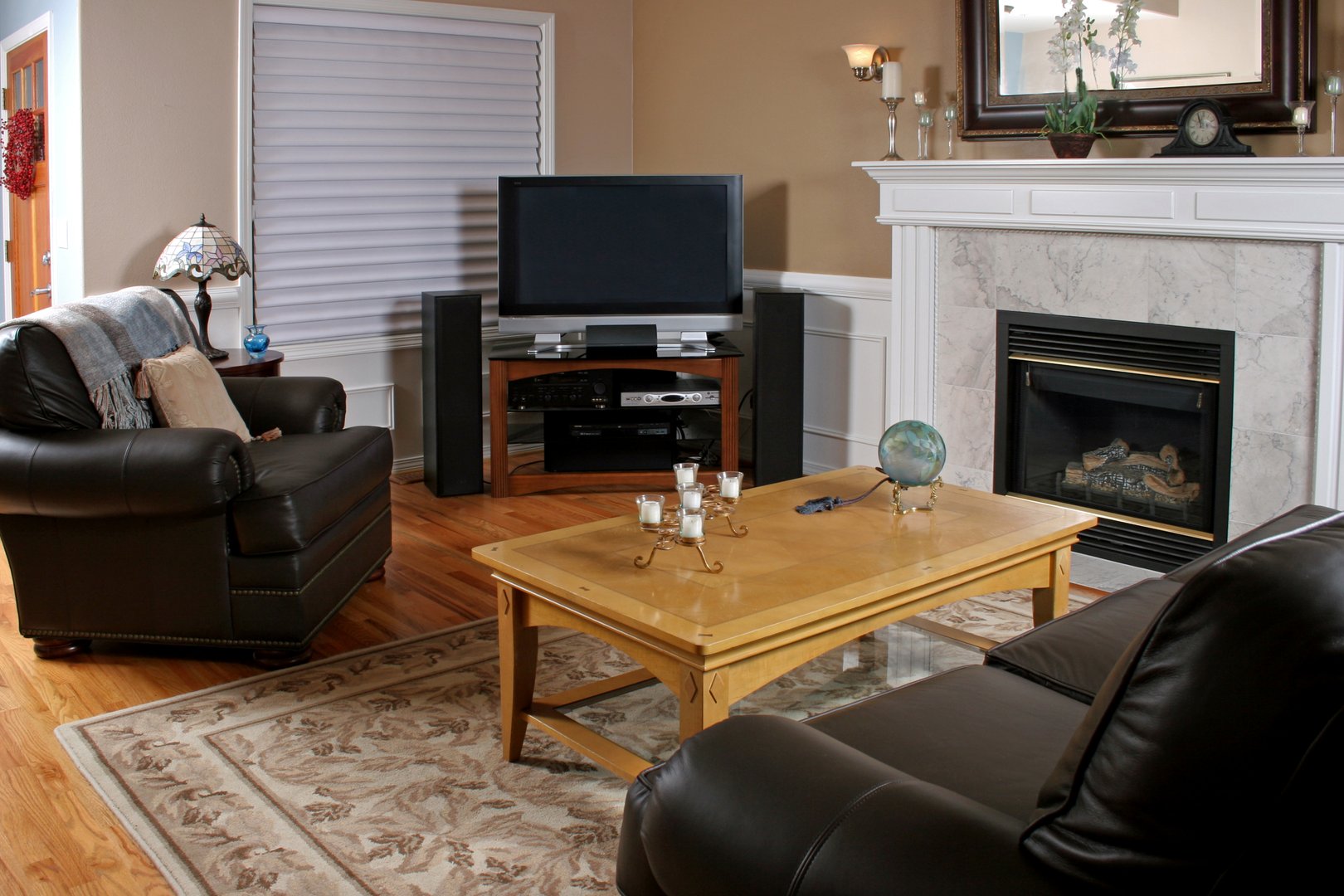 Living room with leather chairs, a TV, fireplace, wooden coffee table, and decorative items on a rug-covered hardwood floor.