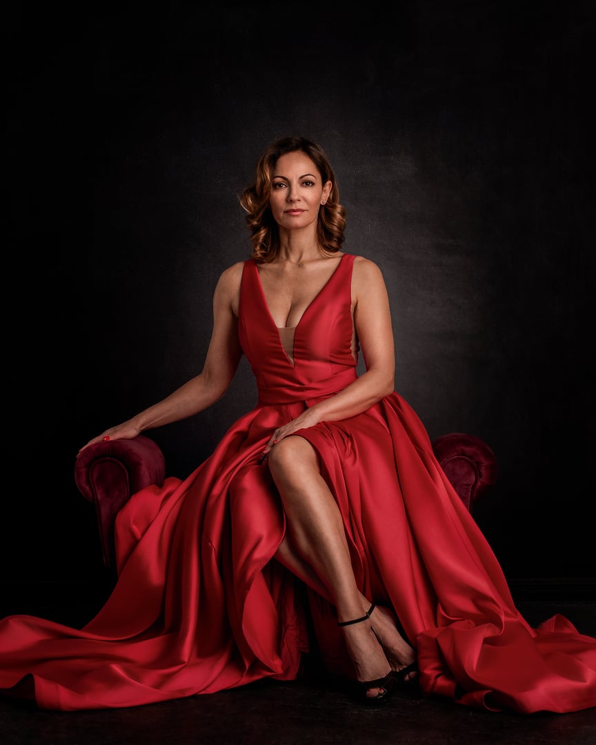 Attractive mid aged woman wearing red gown. Blond haired female looking at camera and smiling against isolated dark background.