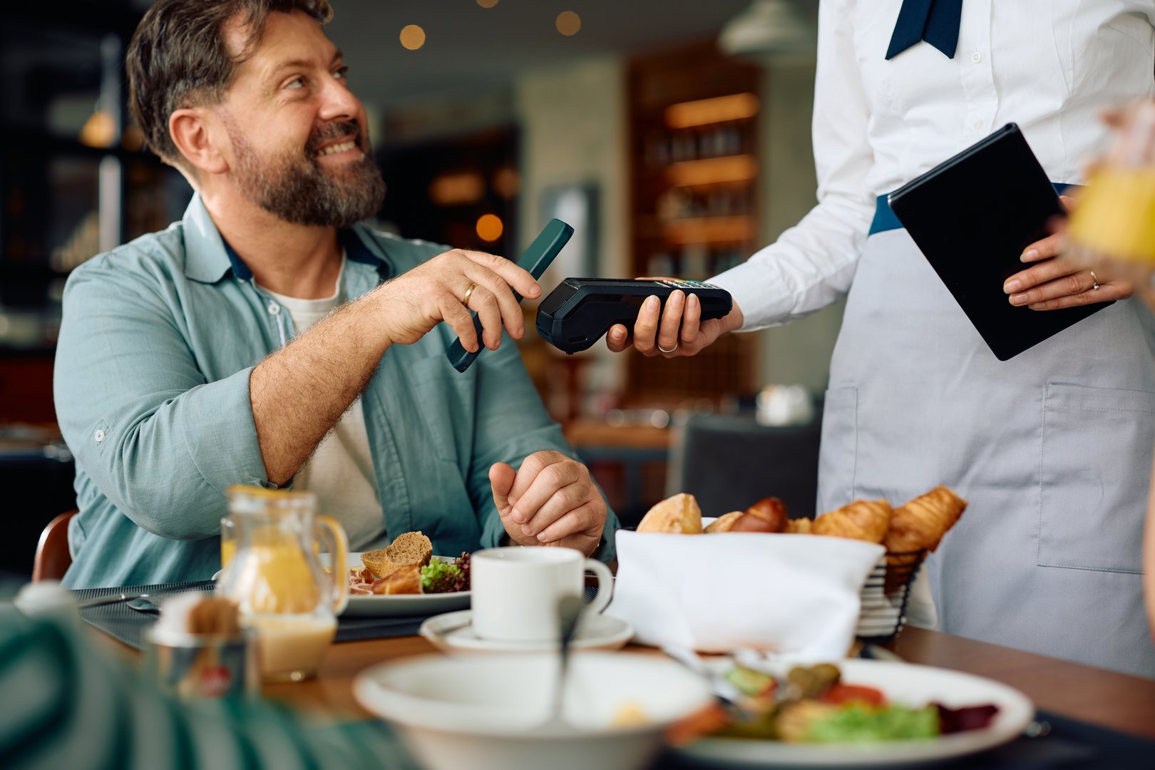 Close up of man using smartphone while paying to a waitress in a restaurant