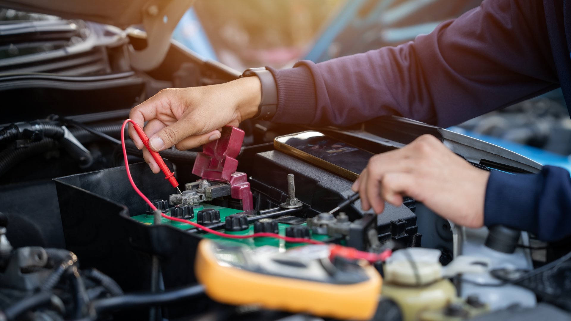 A mechanic is working on a car engine. He uses a multimeter to check the battery.
