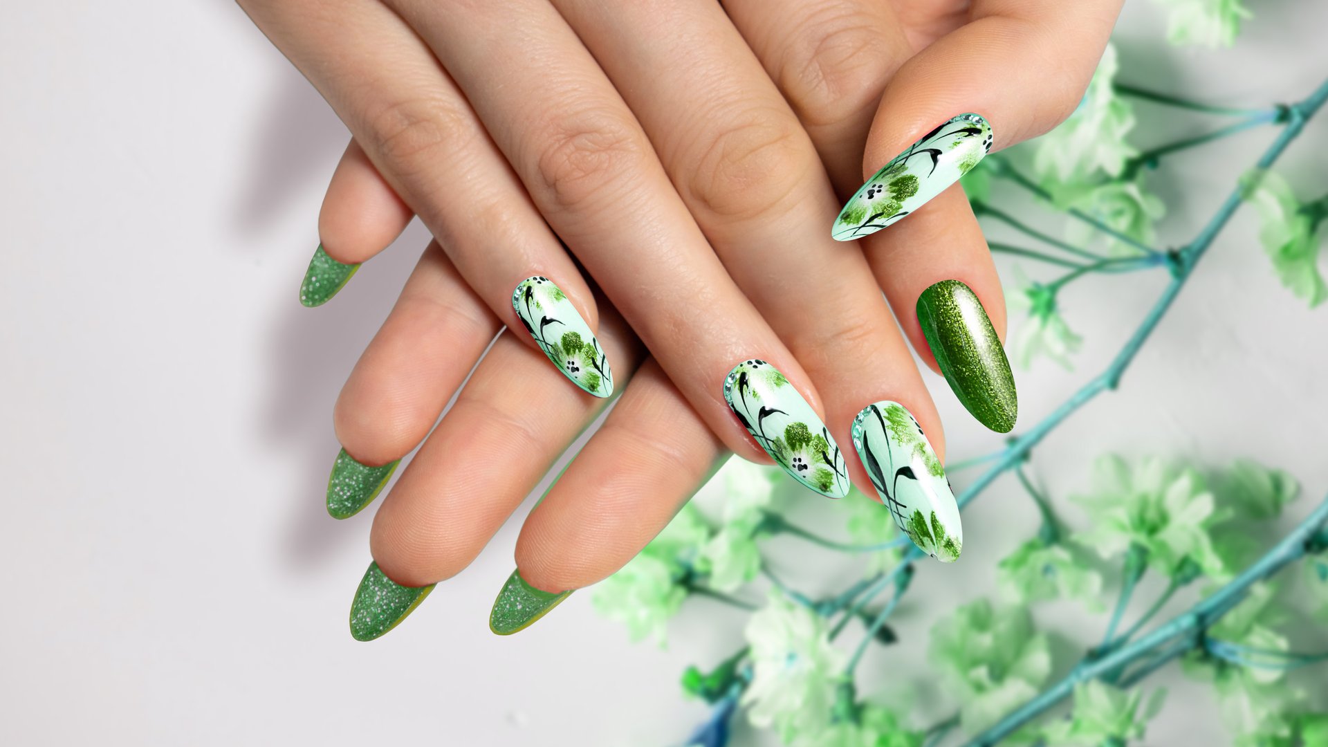 Flower nail design. Green manicure on sharp, long nails close-up on a flower background with painted flower design.