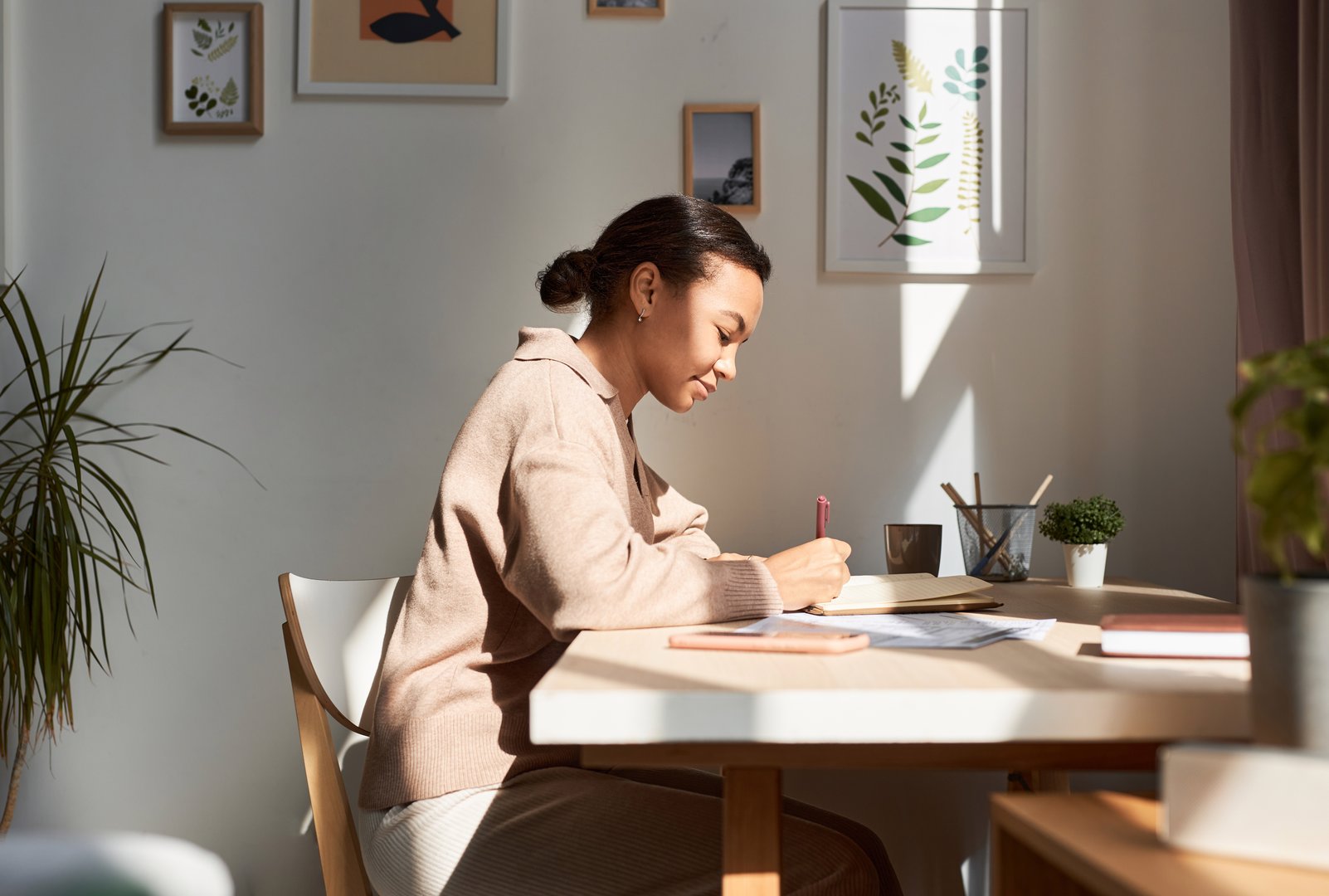 Minimal side view portrait of young African American woman writing in notebook at home with sun rays, copy space