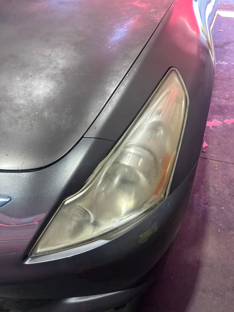 Close-up of a car's front headlight with a slightly worn appearance and nearby matte black hood.