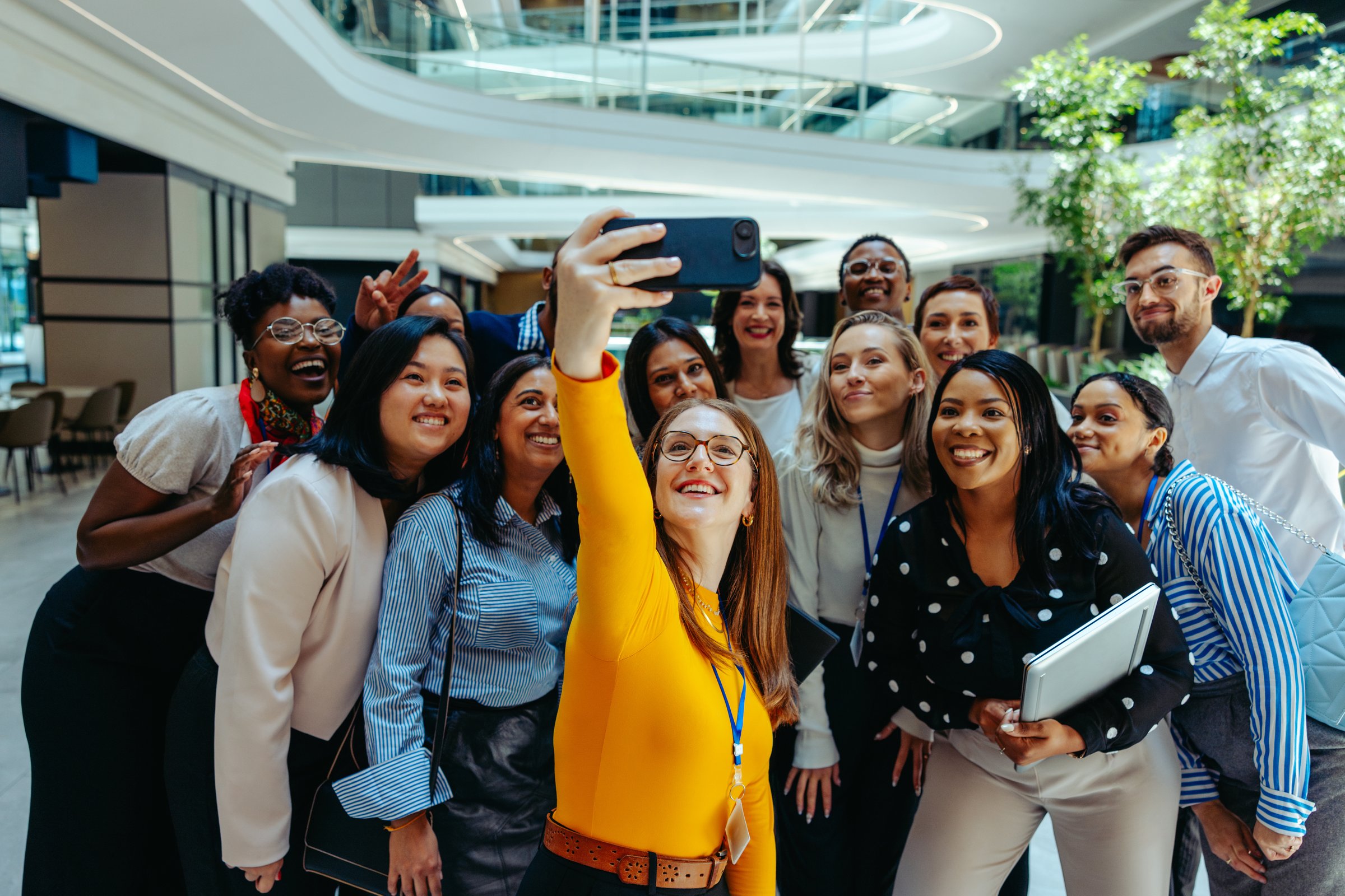 A diverse group of colleagues take a joyful selfie together. The setting is vibrant and filled with natural light, creating a warm and friendly atmosphere. This image captures a moment of team bonding.