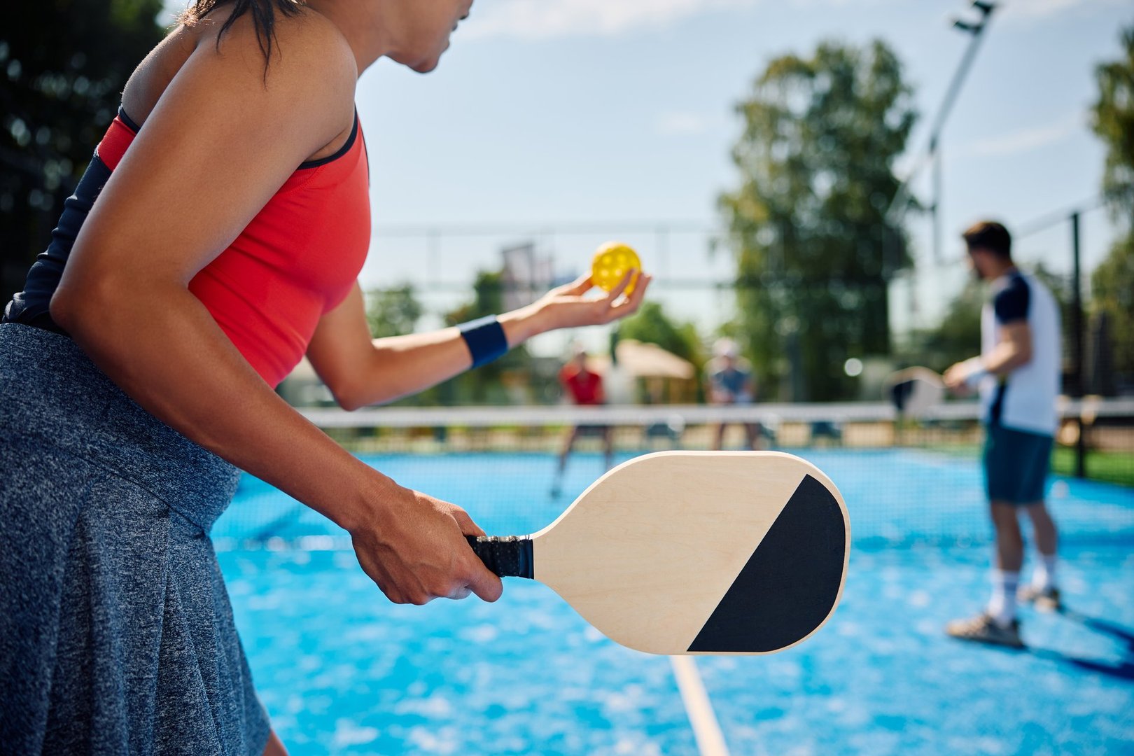 Unrecognizable African American woman serving the ball while playing mixed doubles in pickleball.