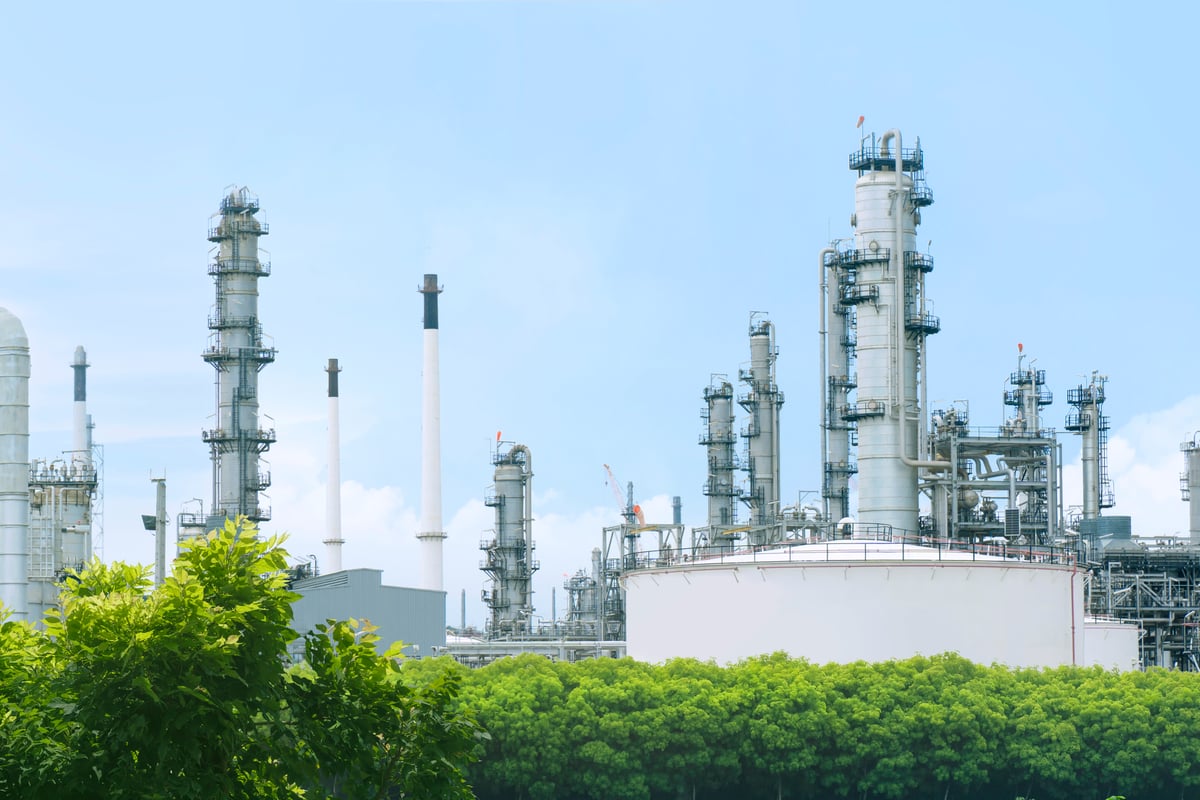 Oil refinery plant from industry zone with lush green trees and blue sky, large Oil and gas petrochemical industrial, Refinery factory oil storage tank and pipeline, Ecosystem and good environment.