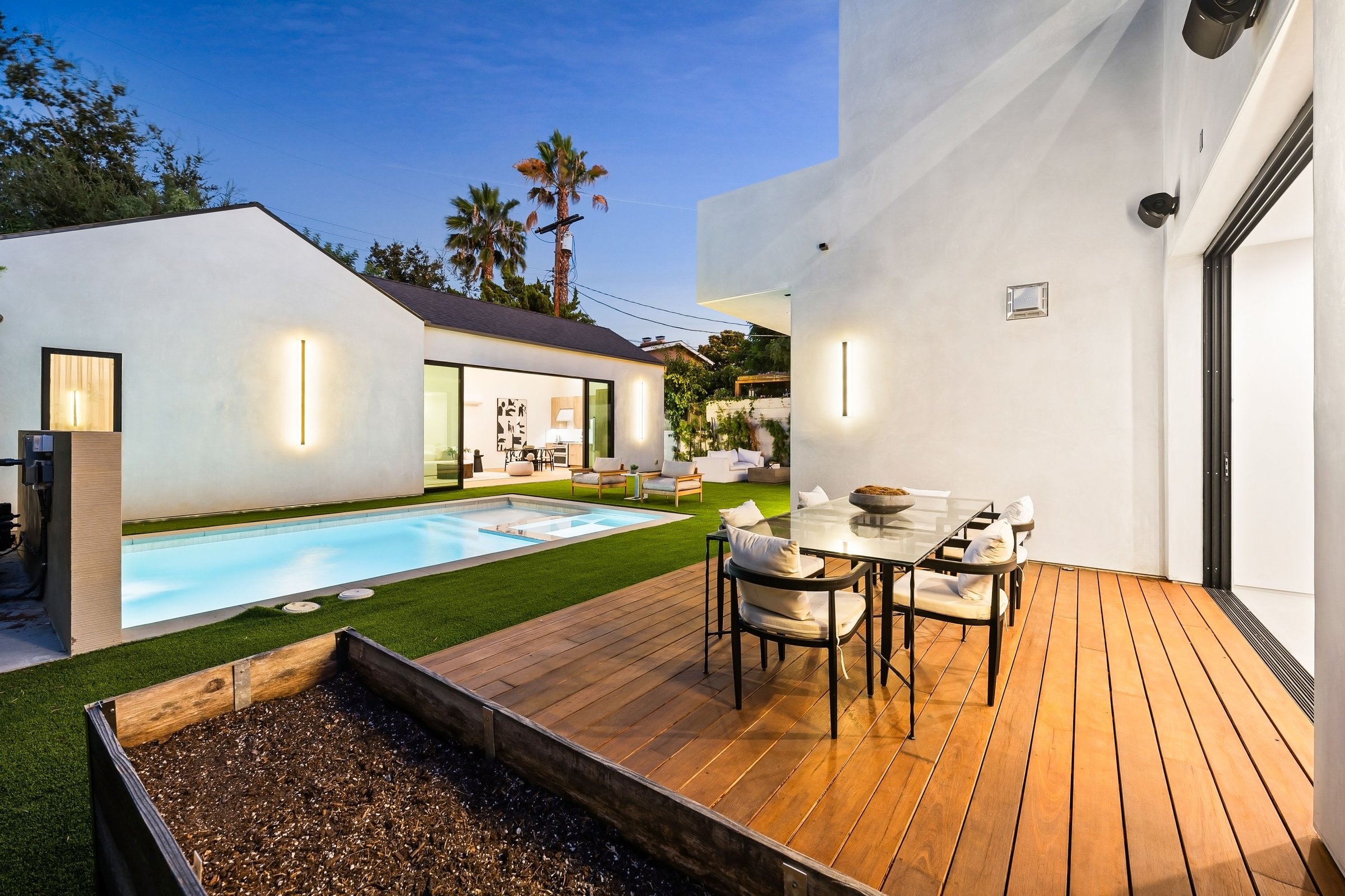 Modern backyard featuring a swimming pool, wooden deck, and outdoor dining area in a contemporary home setting.