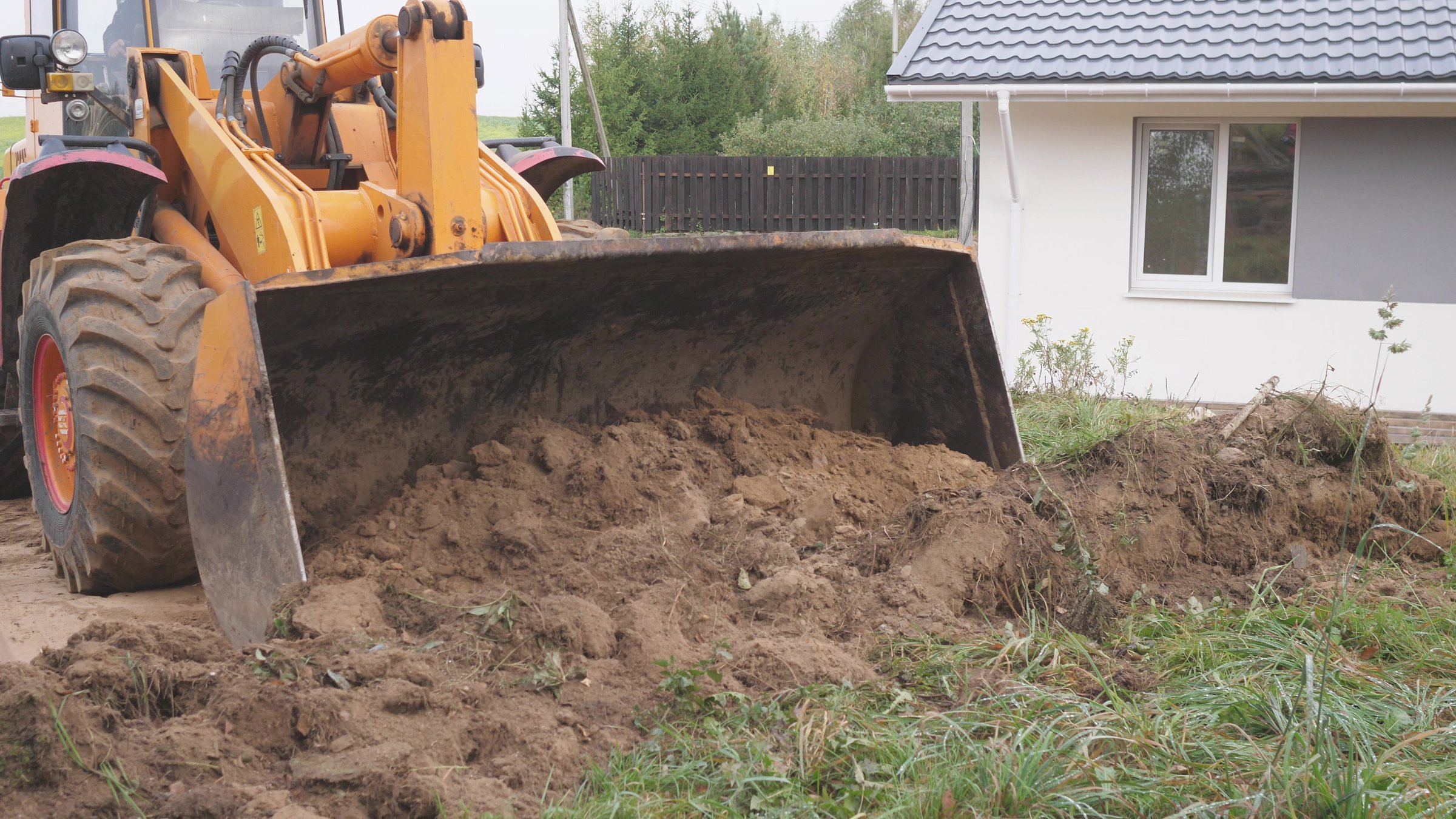 A bulldozer is actively moving dirt within a residential area, as it prepares for upcoming construction work