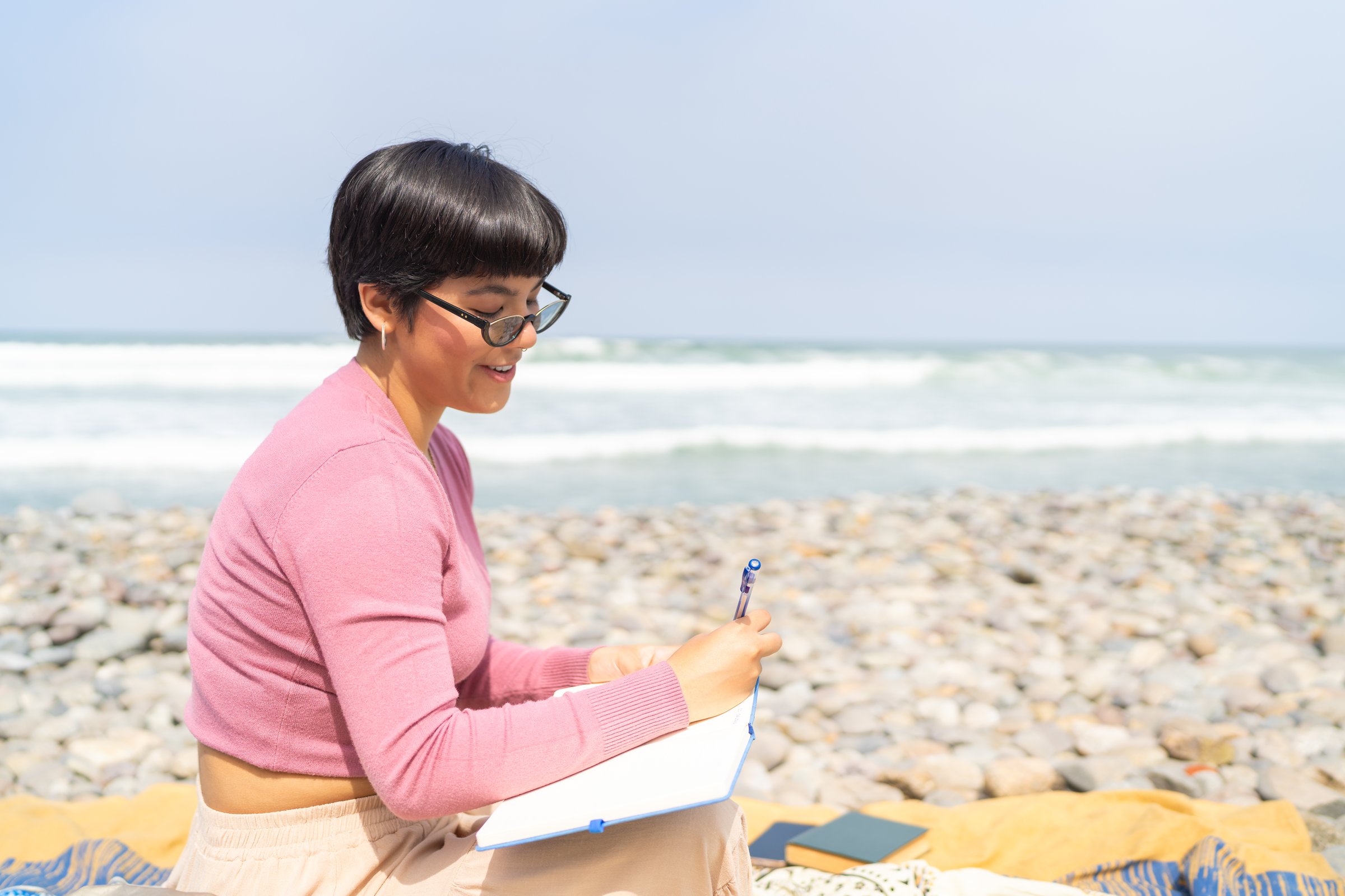 Profile photo of a latin woman writing a diary sitting on the beach