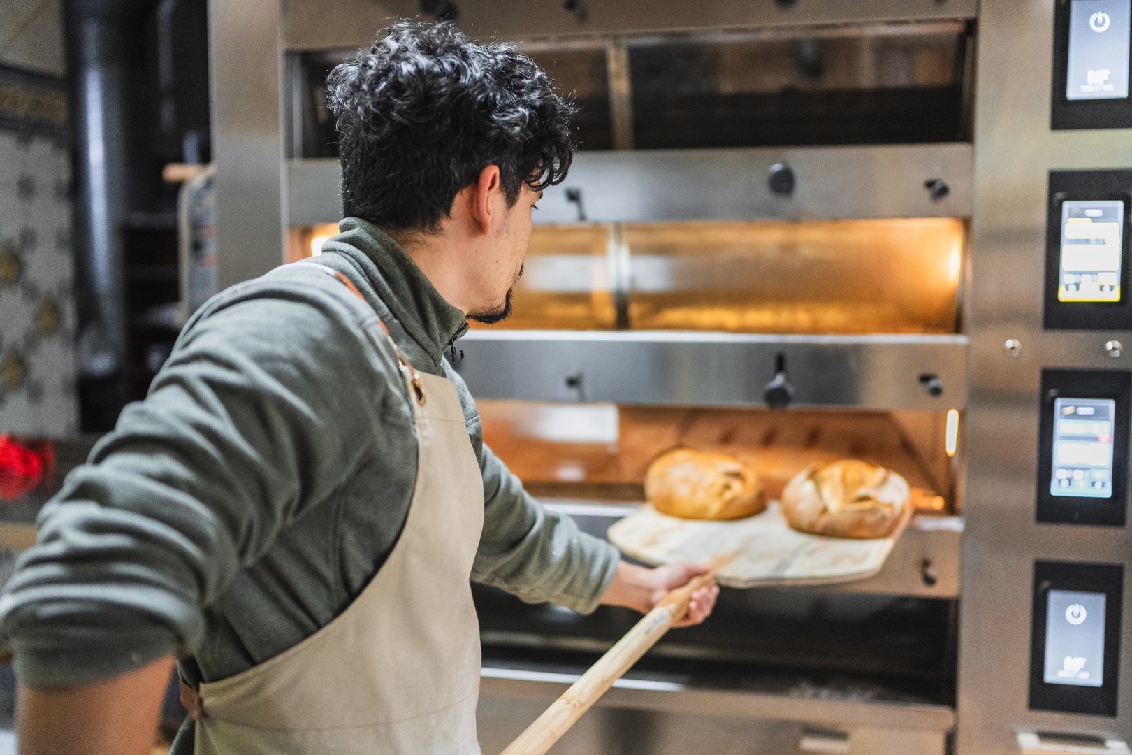 Baker removing two loaves of freshly baked bread from a professional oven