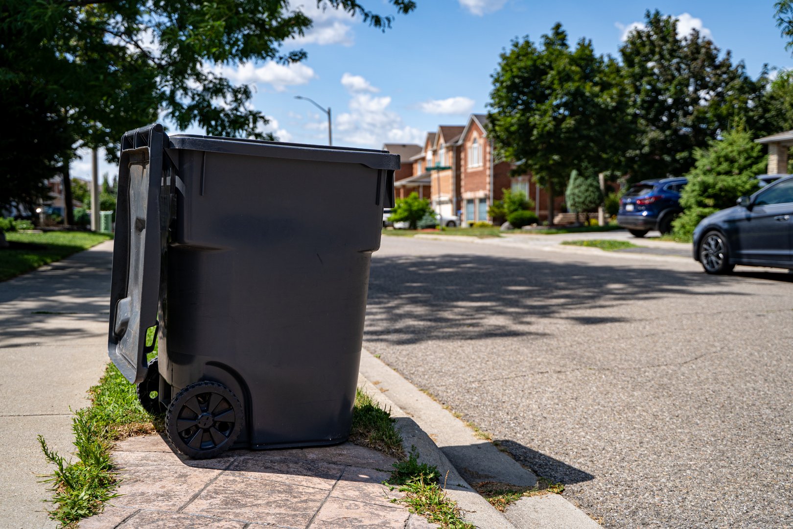 Black garbage bin on suburban street sidewalk.