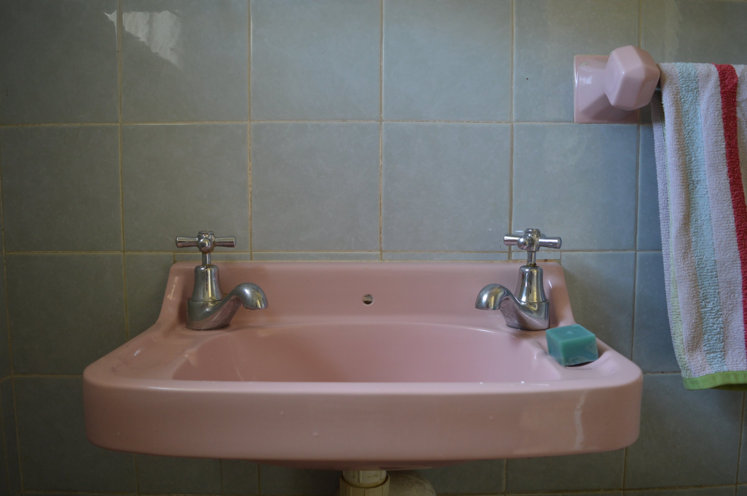 Pink bathroom sink with separate hot and cold taps, a blue soap bar, and a striped towel hanging on a pink holder.