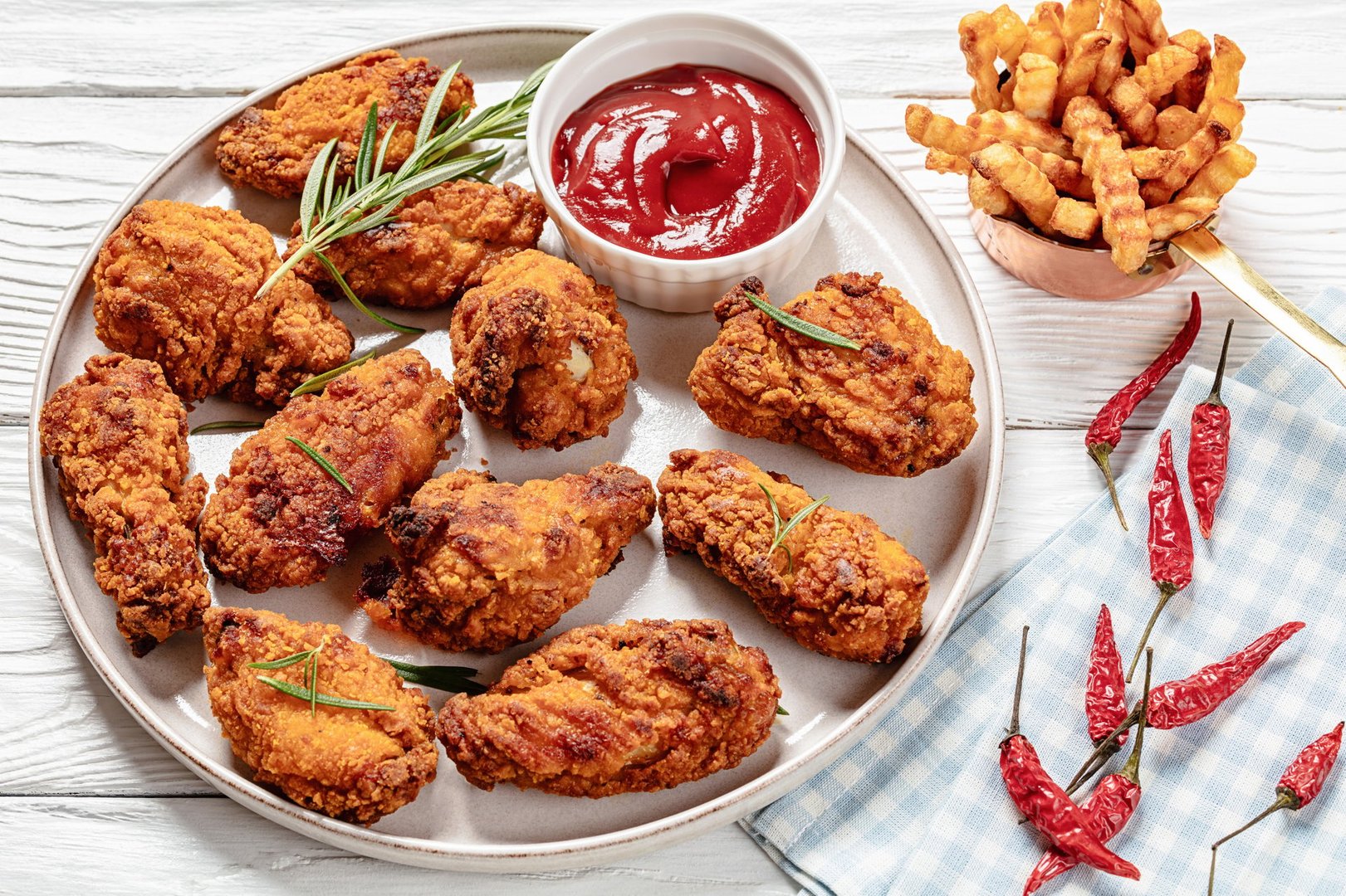 american style crispy fried chicken wings on plate with ketchup, french fries on white wooden table, landscape view, close-up