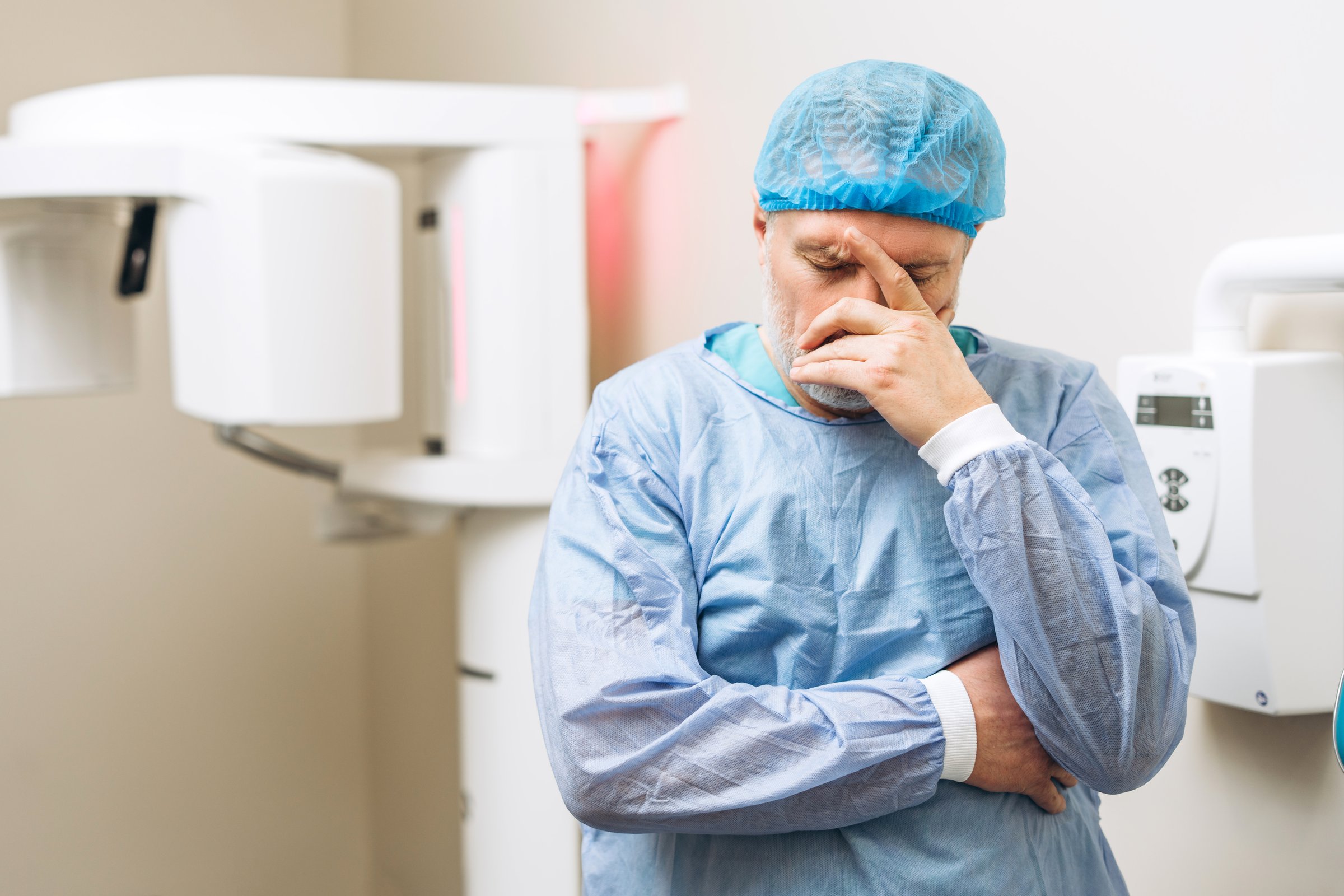 Portrait of upset mature male covering face by hand standing in X-Ray room at hospital. Dental treatment, radiology, panoramic scanner