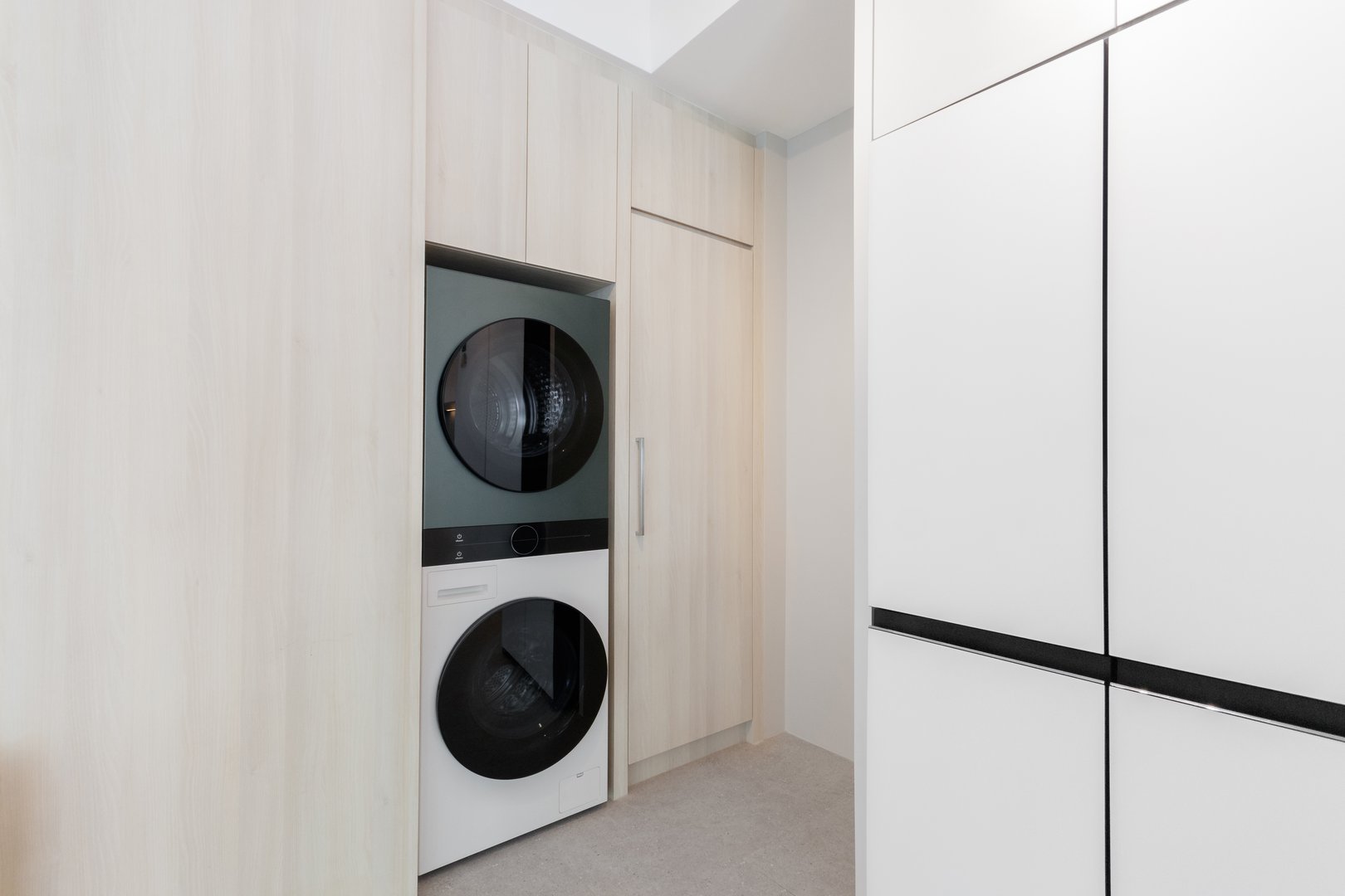 modern laundry area with a sleek stacked washer and dryer fitted into custom wooden cabinetry. Ideal for showcasing efficient, space-saving interior design solutions.