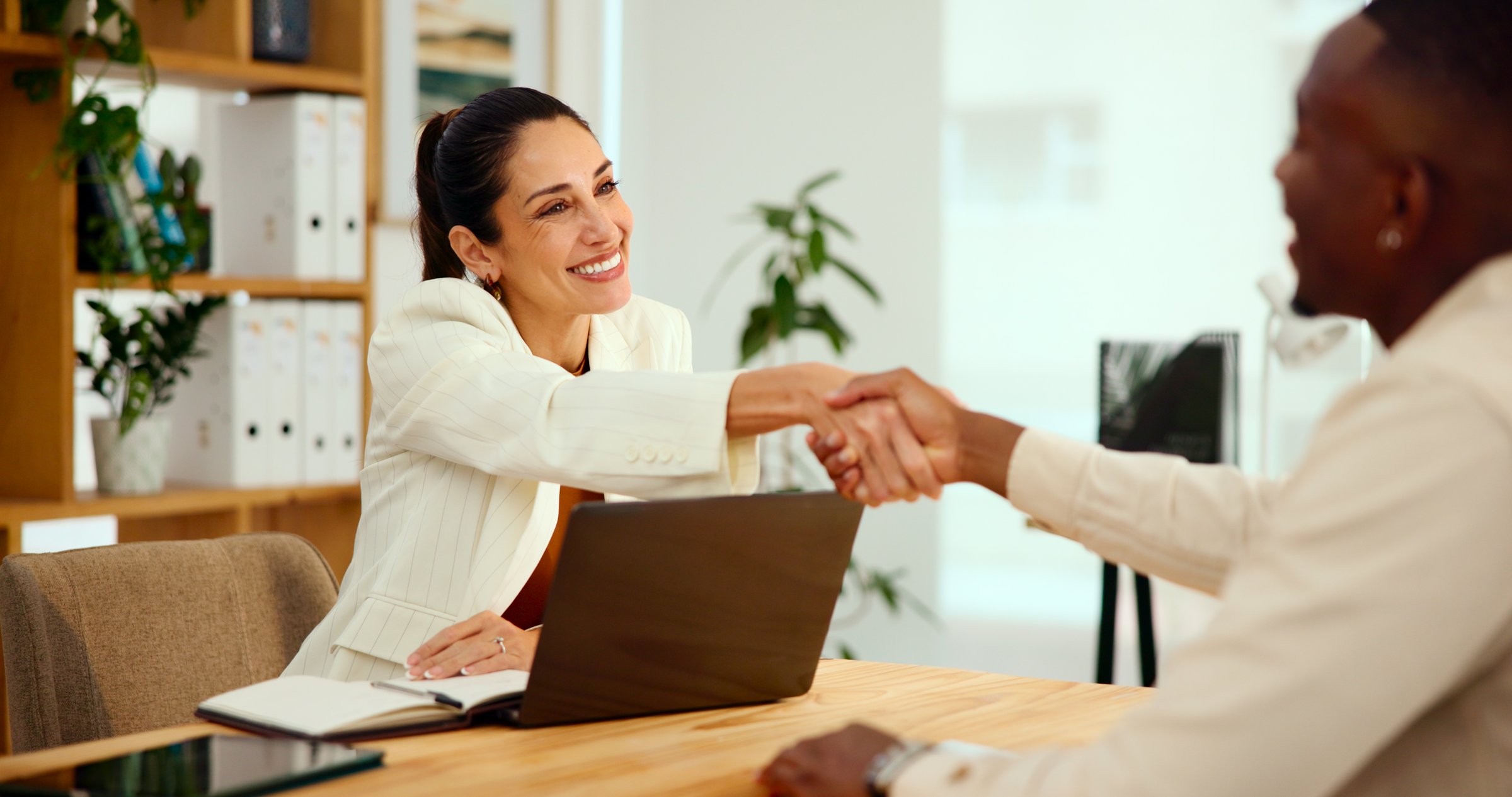Handshake, woman and laptop in office for interview, meeting or onboarding discussion. Applicant welcome, female HR officer and communication for contract information or job requirements in agency