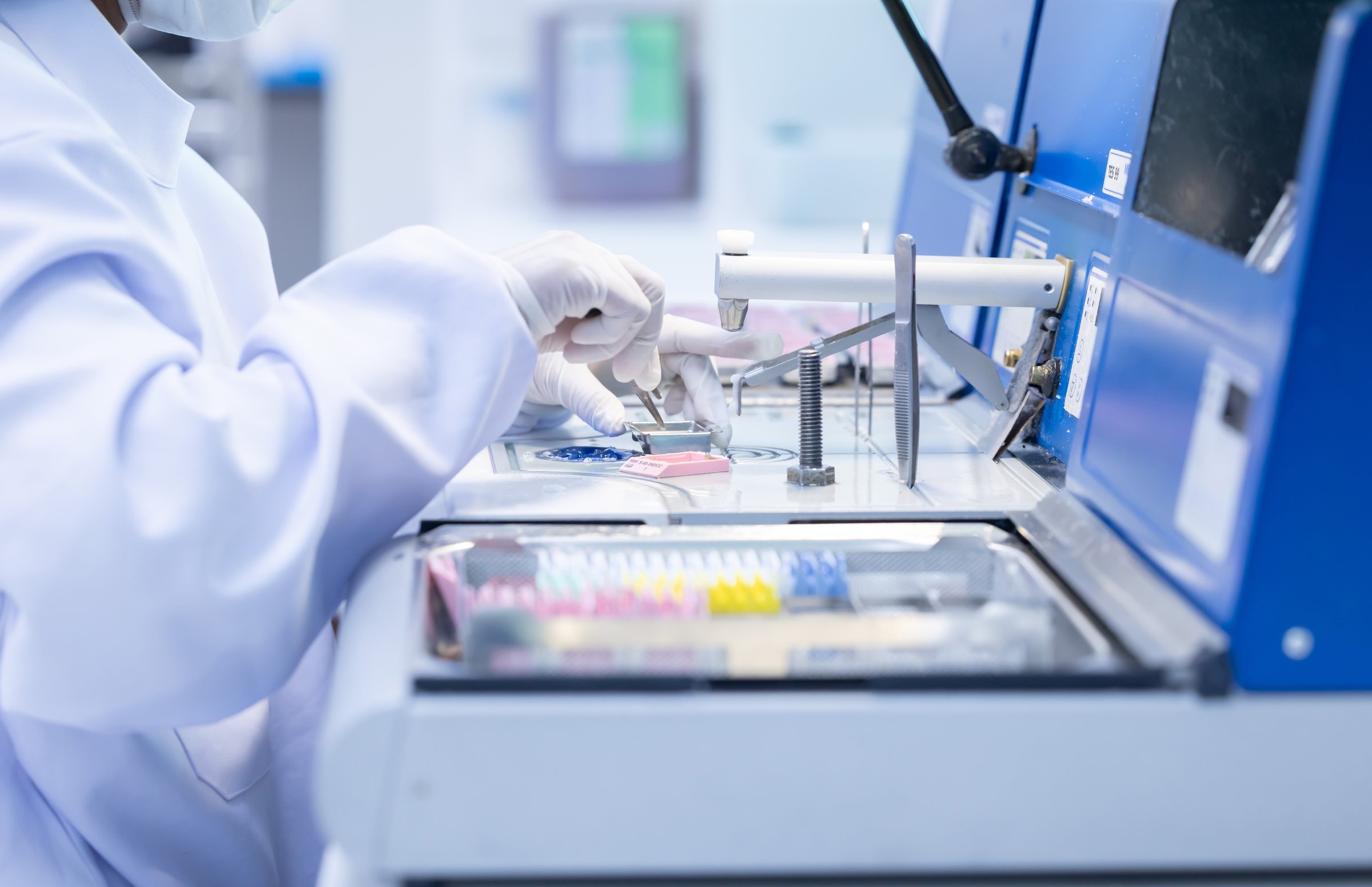 A laboratory pathologist in protective gear operates sophisticated equipment to perform scientific analysis. The setting is clean and organized, highlighting a professional workspace.