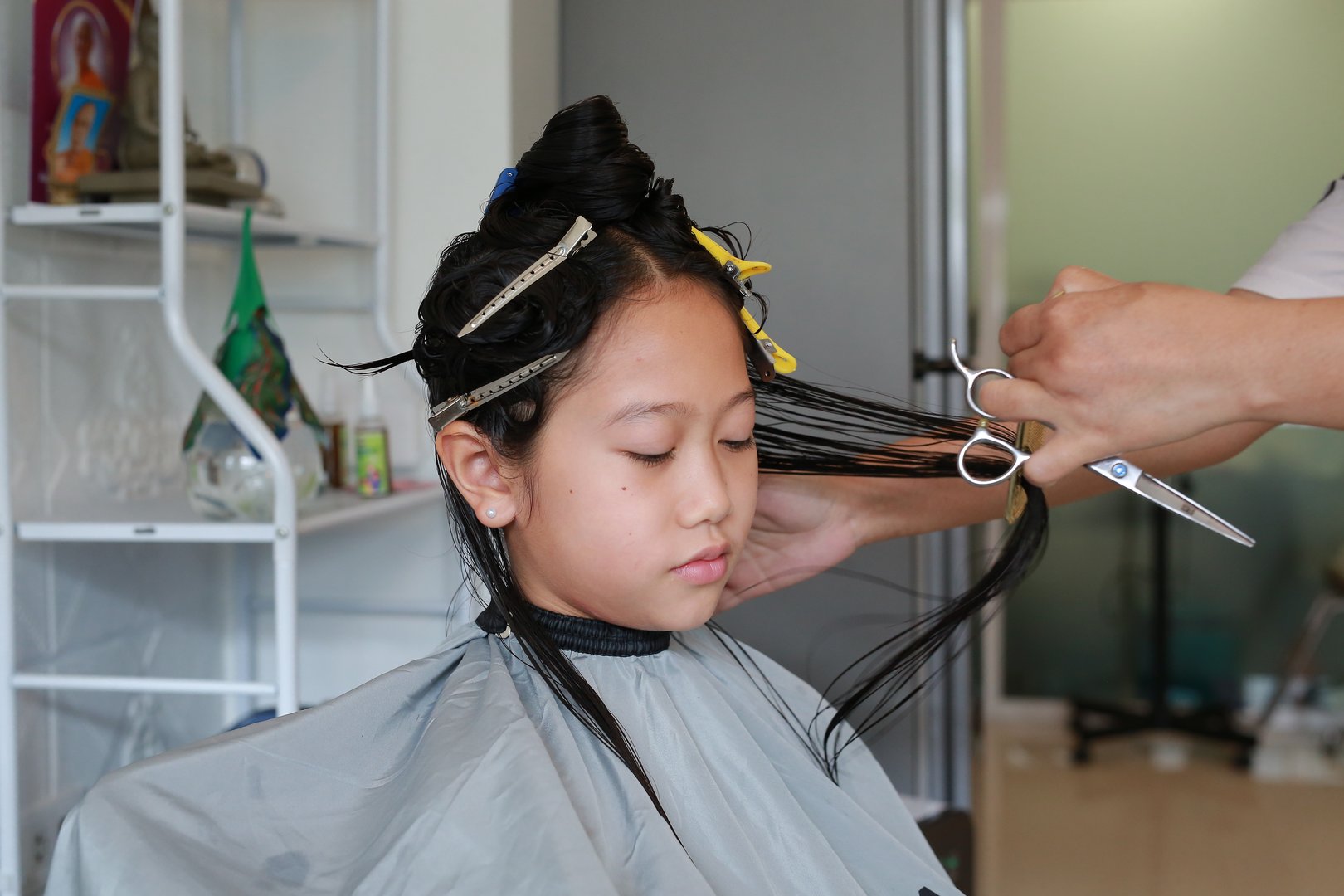 Asian preteen girl having her hair cut. Child sitting in beauty hair salon style for children. Close-up.