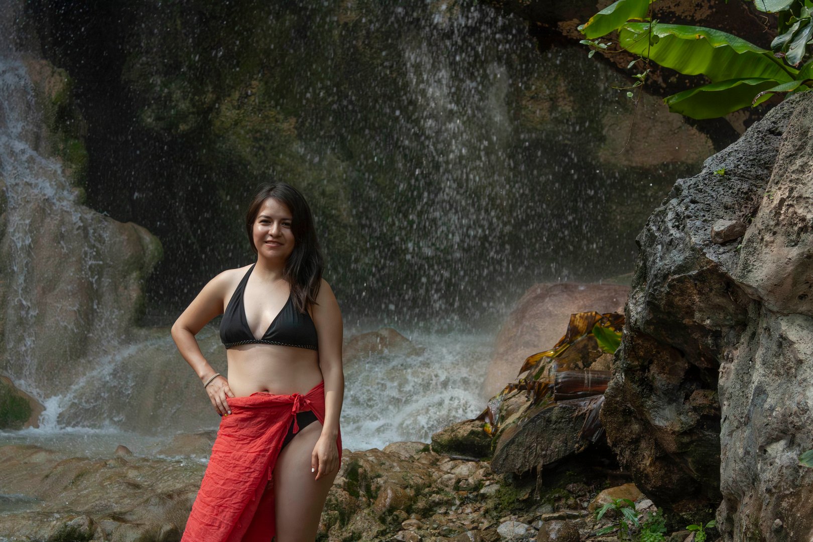 Woman enjoying the cool breeze next to the fresh water waterfall natural environment moss rocks and water in Hidalgo, State of Mexico.