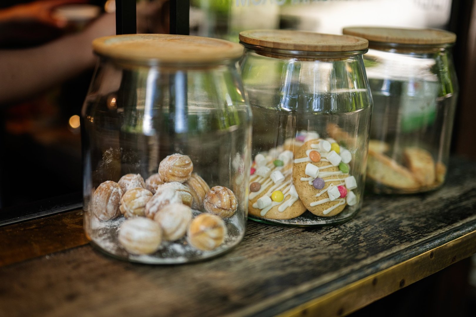 Three glass jars displaying assorted cookies and biscuits placed on a wooden surface.