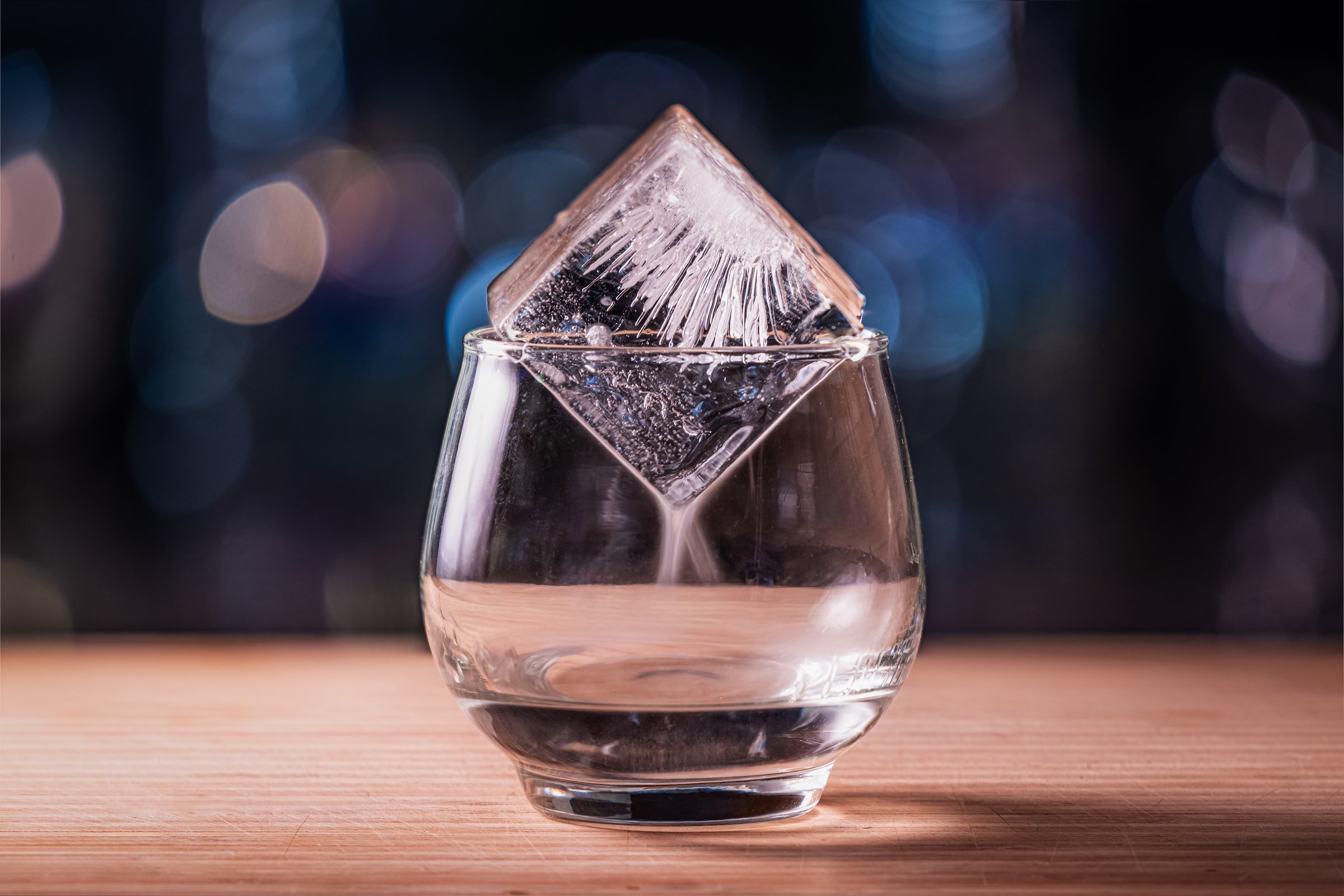 Close up of a clear glass topped with ice with a flaming alcoholic beverage creating a fog from the different temperatures
