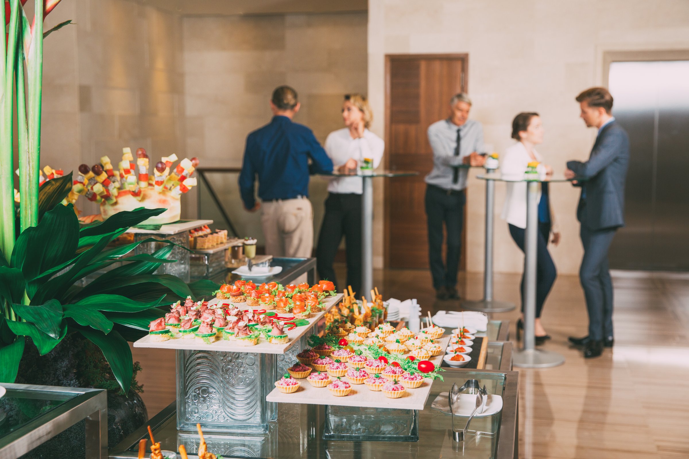 View of different canapes, tartlets and snacks on buffet table in restaurant. Business people eating and talking in background. Catering concept