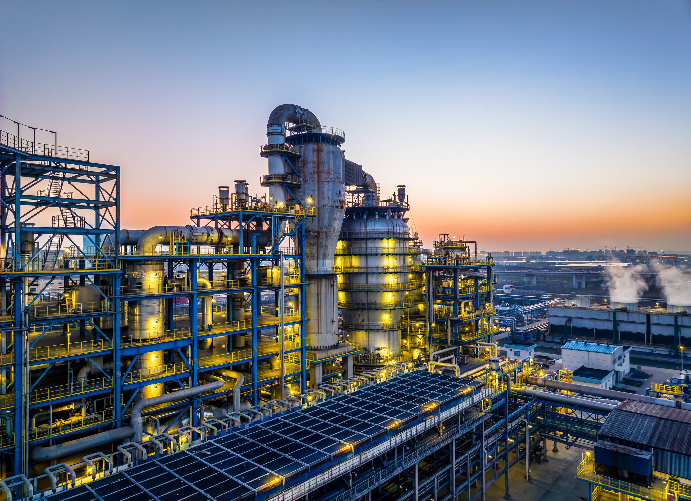 Features lit-up oil refinery and chemical plant, showcasing complex industrial structures and energy production in the evening.