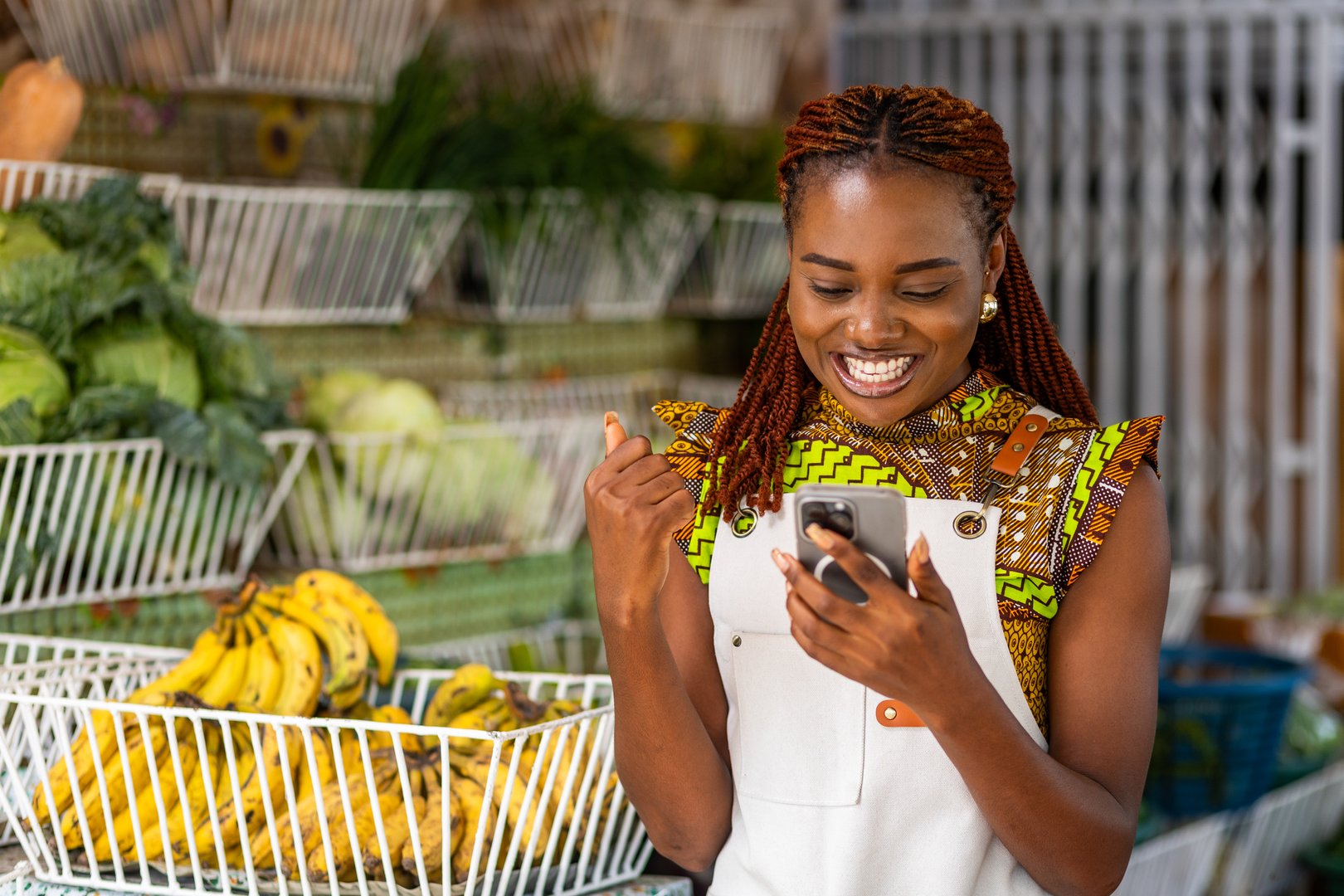 Successful African female small business owner excited, celebrates with joy looking at her smartphone at her local grocery store.