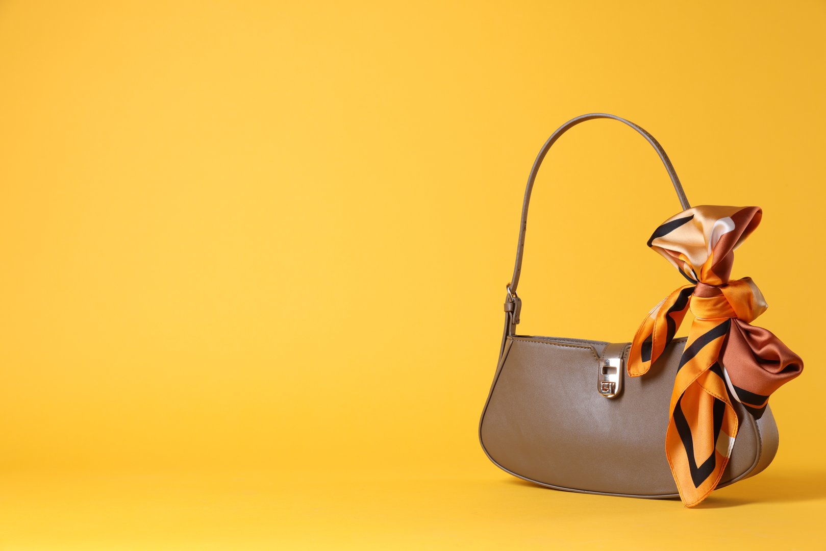 Stylish brown leather bag with handkerchief on yellow background, space for text