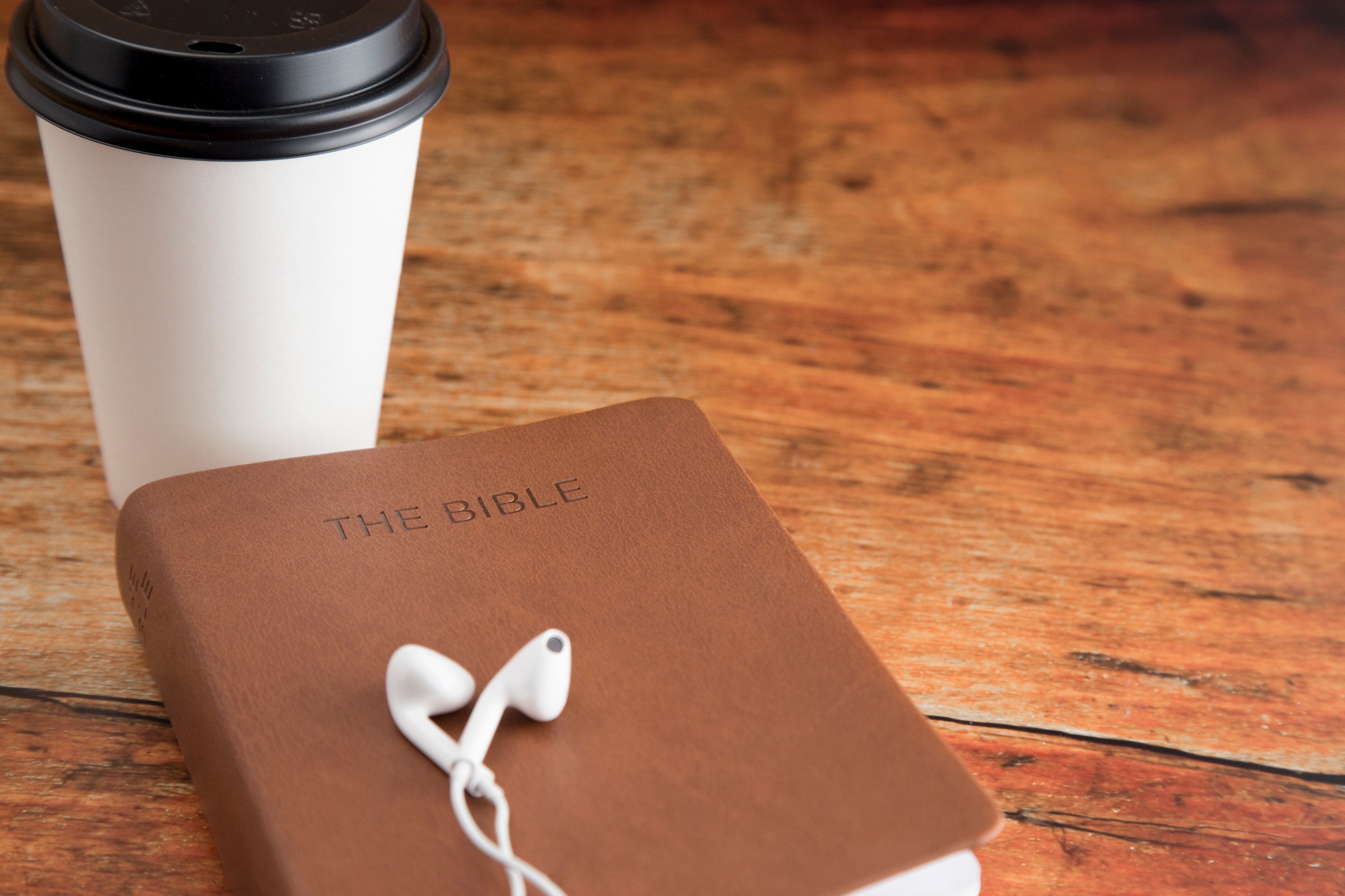 Physical Bible and a Smart Phone with Earphones on a Wood Table