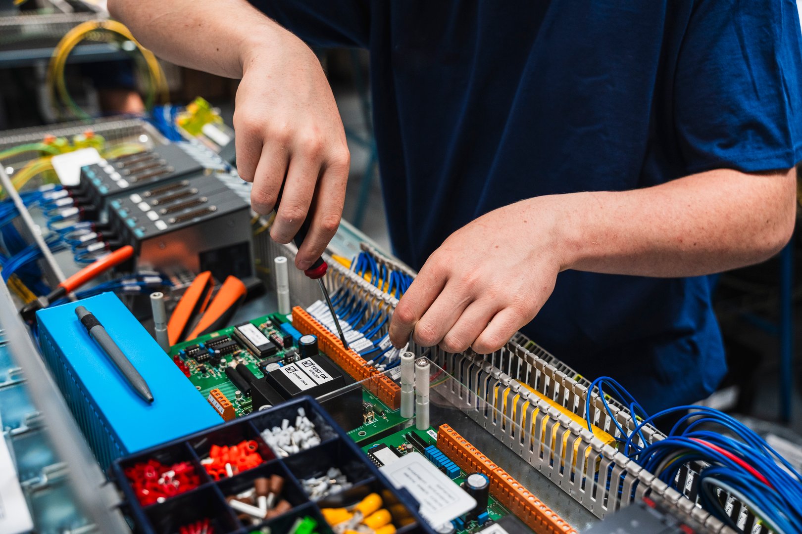 A close-up of a technician's hands working on an industrial electrical control panel. The image shows precise manual work with wires and electronic components, representing concepts such as engineering, electricity, maintenance and automation.