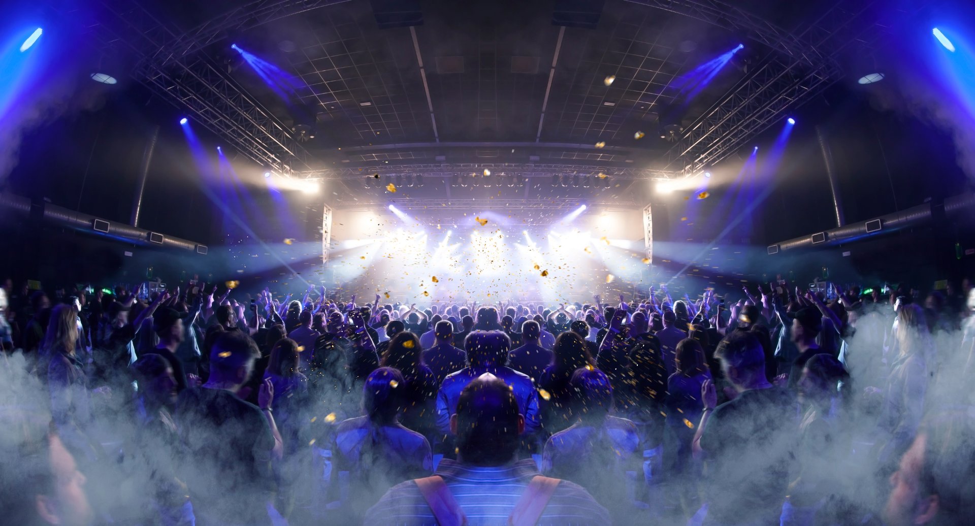 Concert crowd inside a venue, lens flare and smoke are visible.