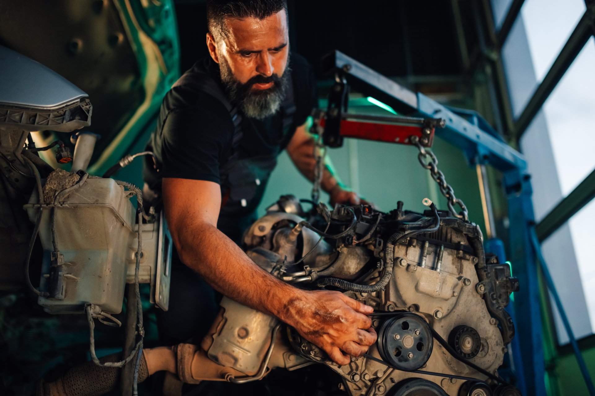 A careful mechanic is examining various car engine parts under bright lighting in a well-equipped garage, showcasing his thoroughness and mechanical know-how.