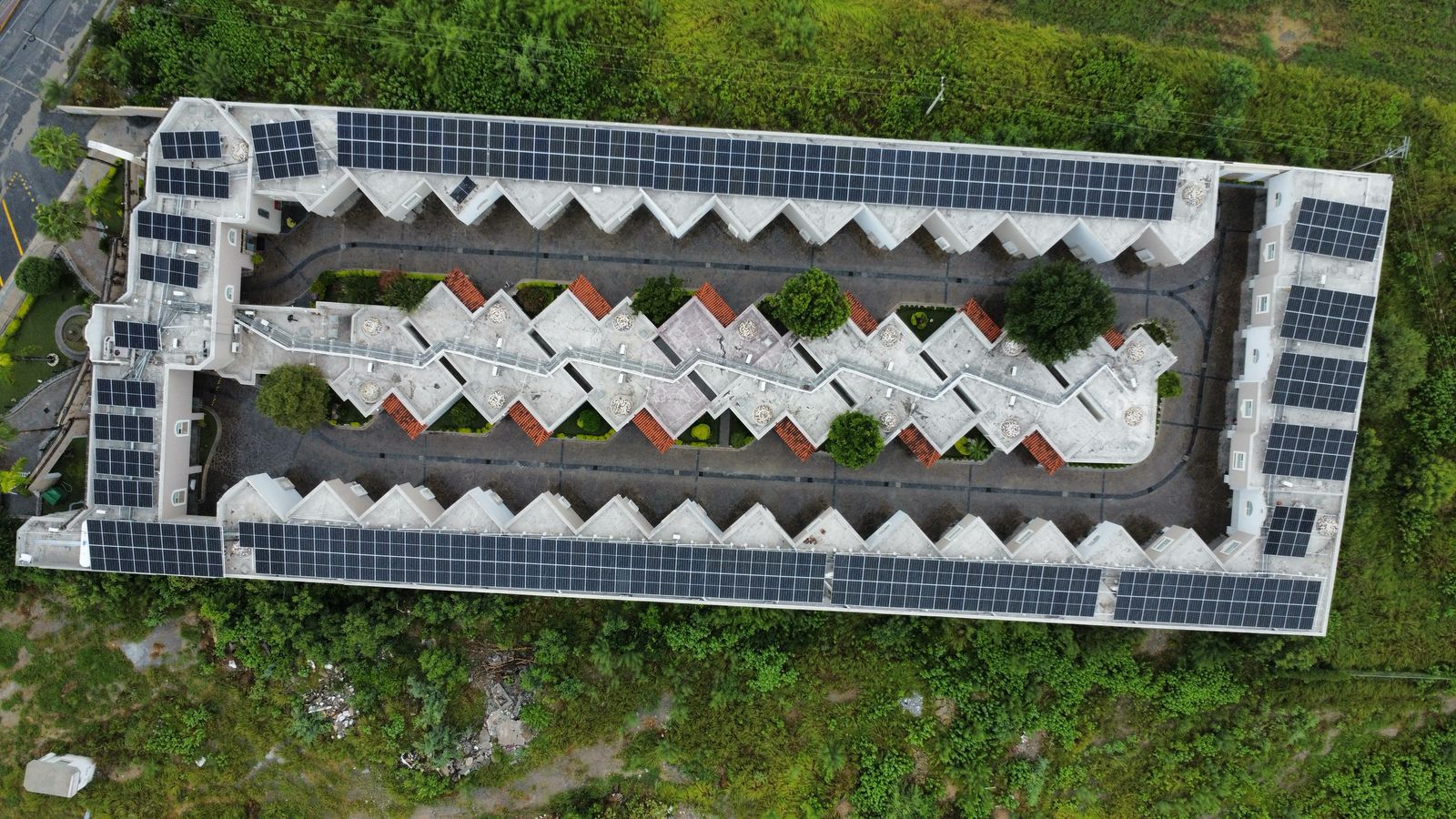 Aerial view of a zigzag-shaped building with solar panels on the roof, surrounded by greenery.