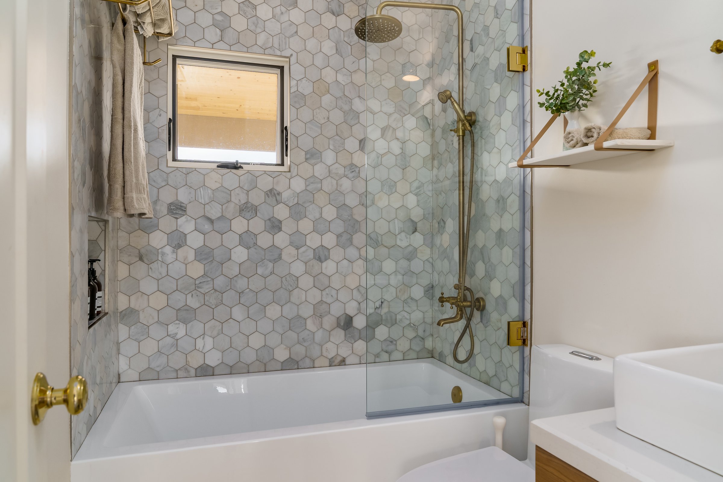 Modern white bathroom with hexagonal tile shower and gold brass fixtures