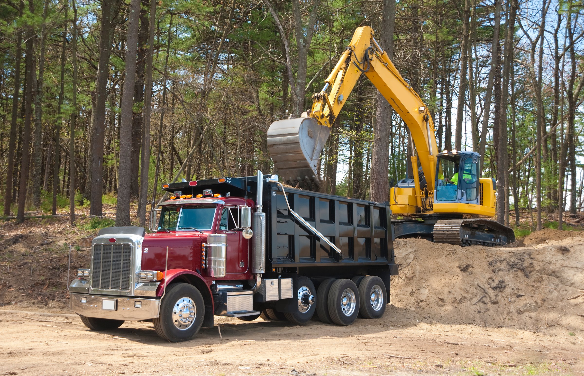 Excavator loading dumper truck with dirt at construction site