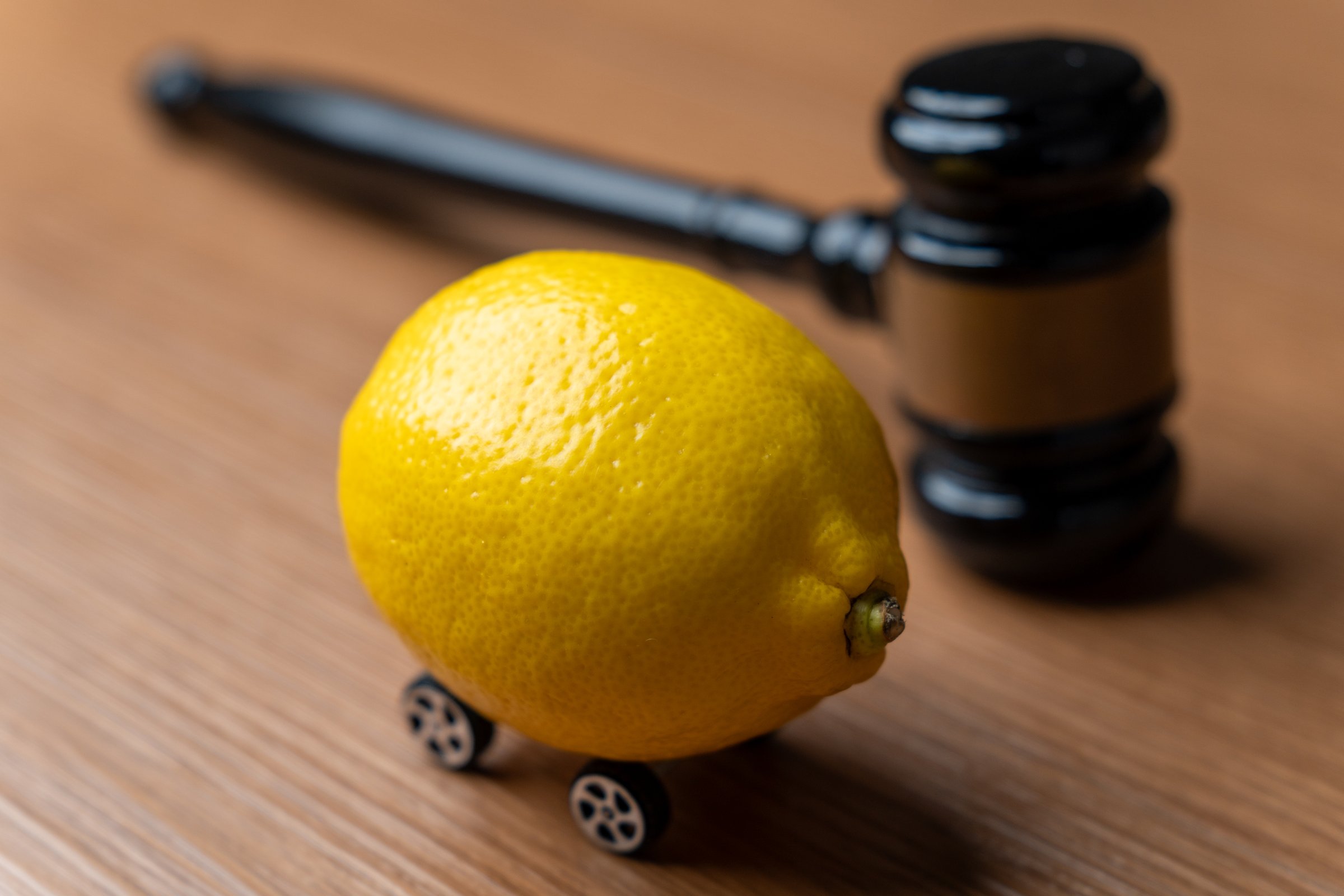 A lemon with small wheels placed near a judge's gavel. Lemon law, defective car, vehicle warranty, or consumer protection issues concept.
