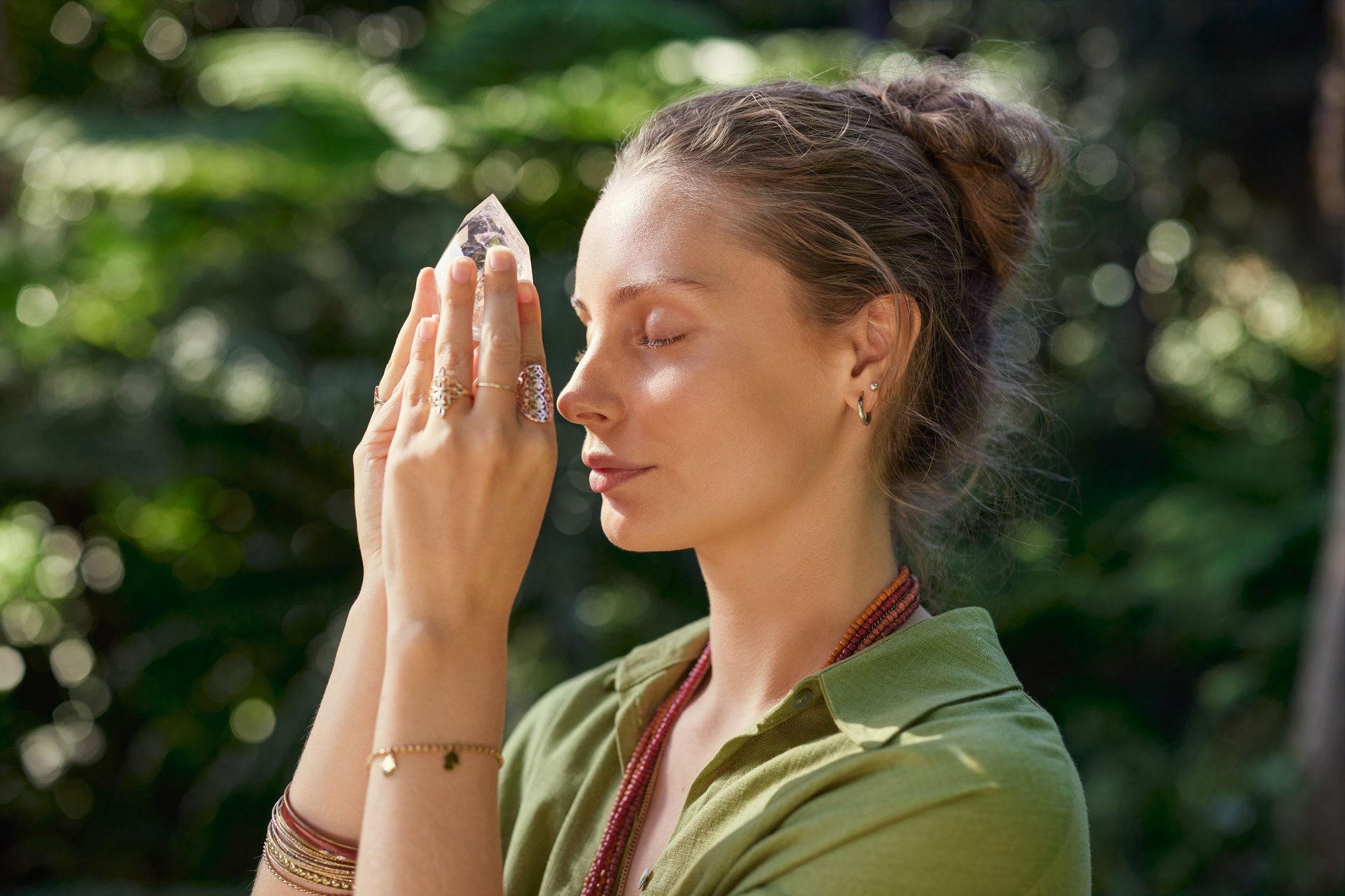 Peaceful woman holding a tower of clear crystal on forehead during meditation in mindfulness retreat, connection with the divine. Woman practicing spiritual healing using quartz crystal to rebalance the chakras and the energies of the subtle body with crystal therapy. Girl connecting with higher energy through crystal, opening of the third eye.