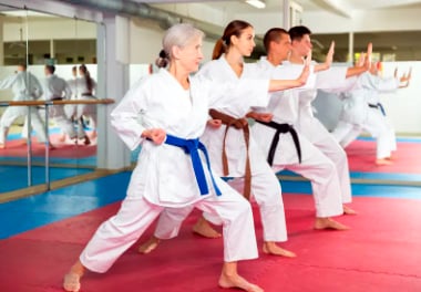 A group of people practicing karate in a dojo, wearing white uniforms with different colored belts, performing a kata.