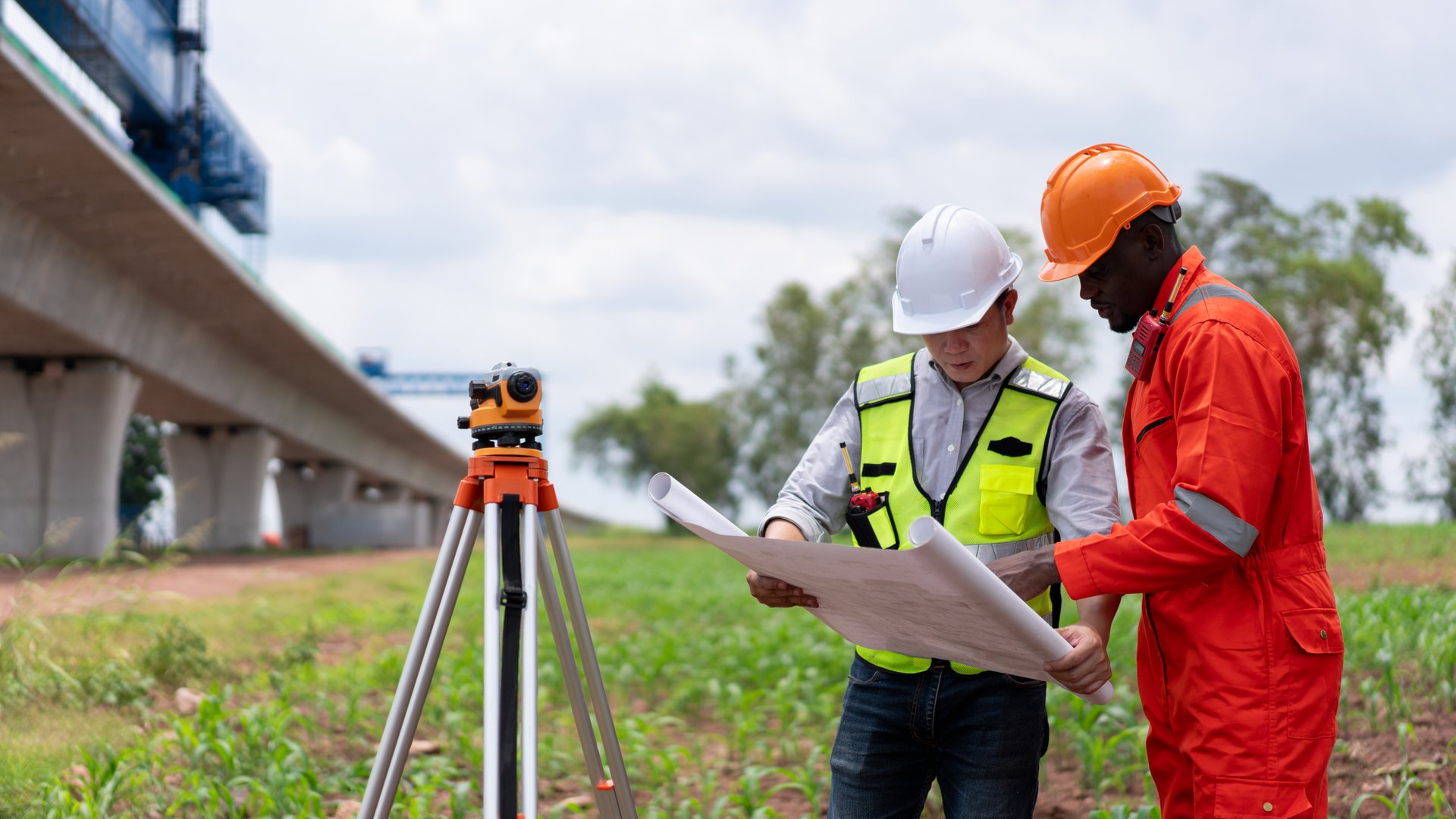 Surveyors and civil engineers using a theodolite and road construction plans to measure and inspect during the building process.