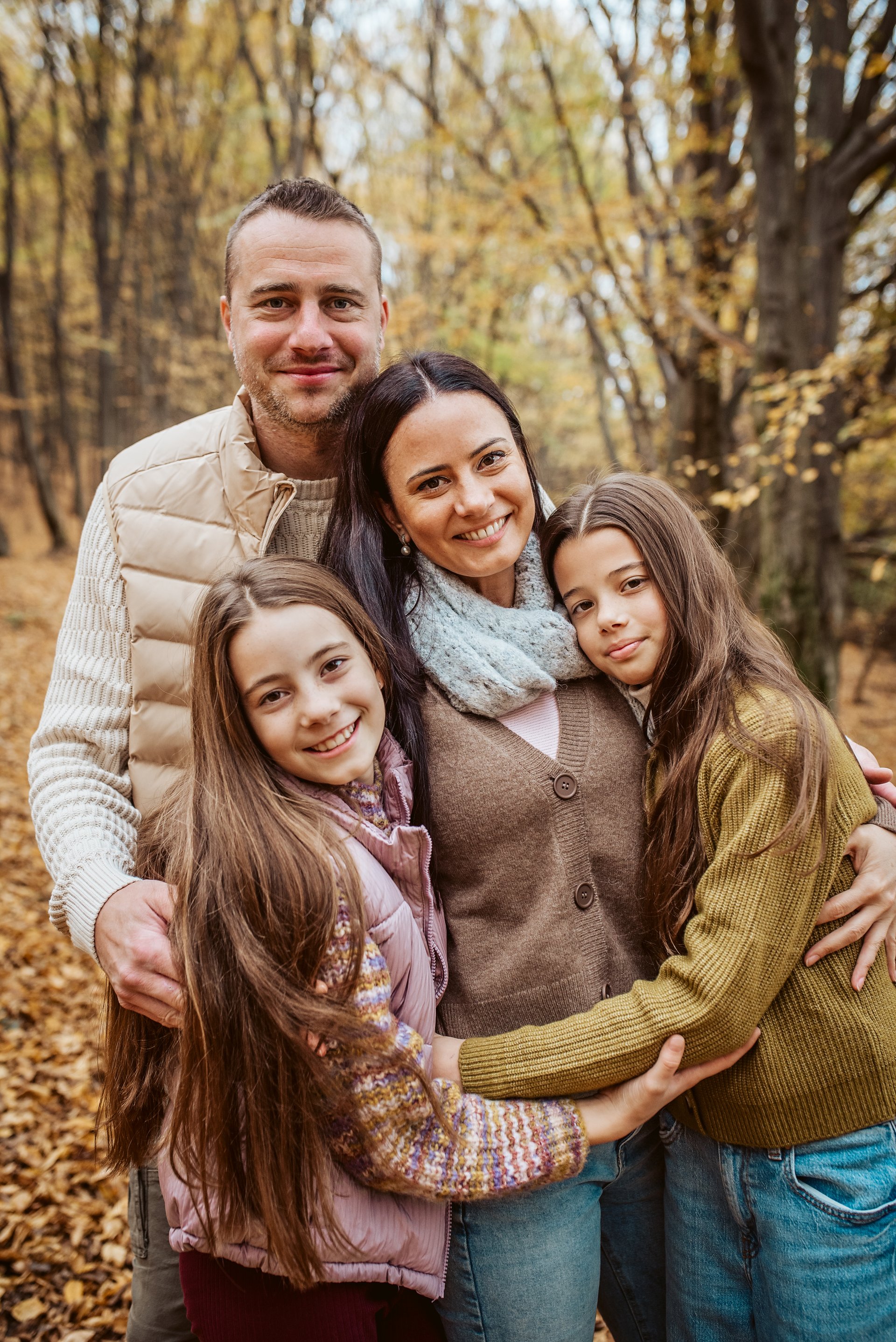 Family portrait of parents with two daughter, standing in the middle of forest. Nuclear family.