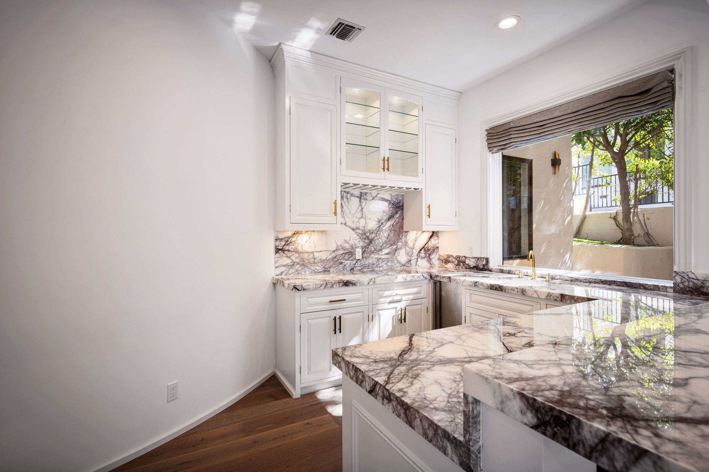A bright kitchen corner with marble counters and large garden-view window