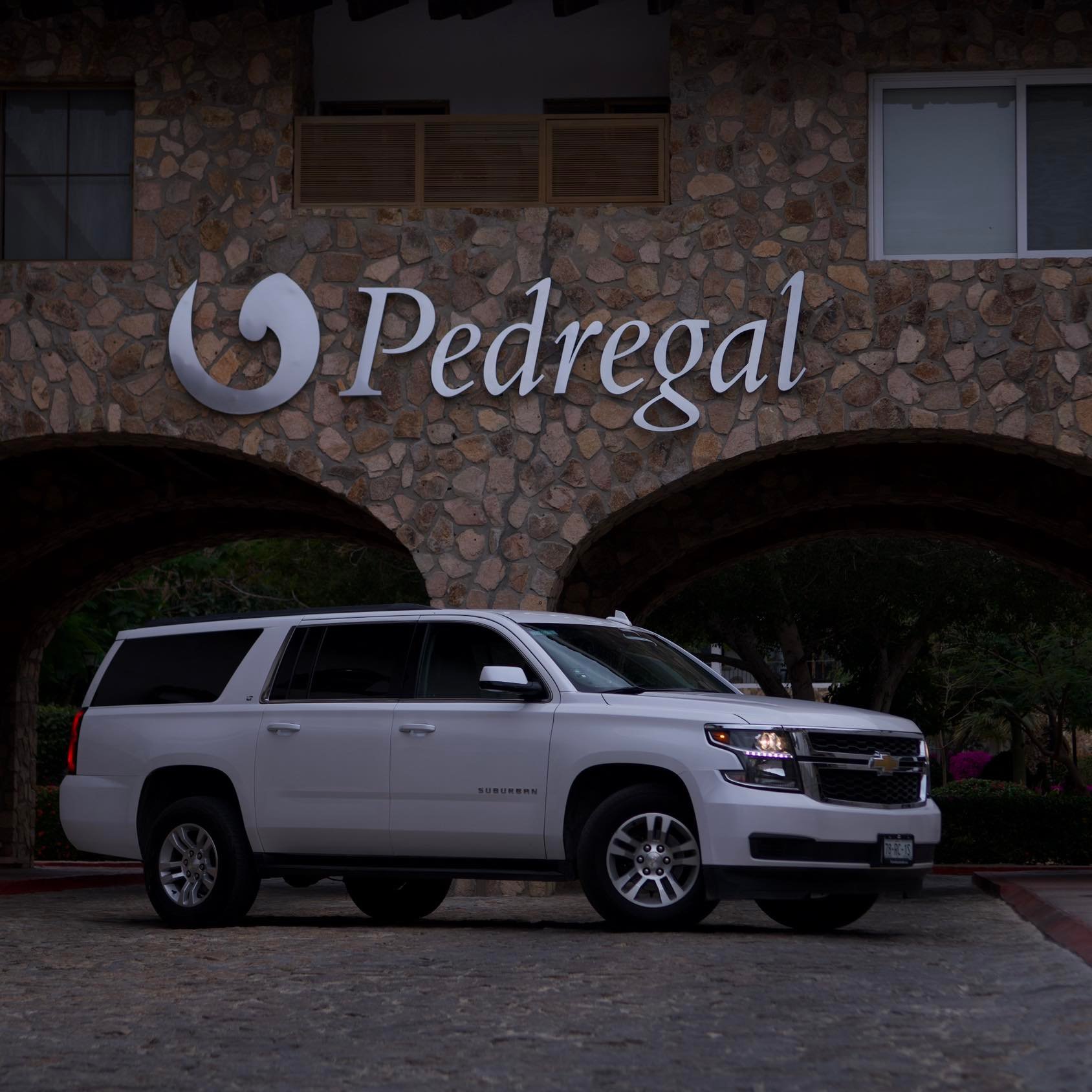 White SUV parked in front of a stone building with the word Pedregal prominently displayed above.