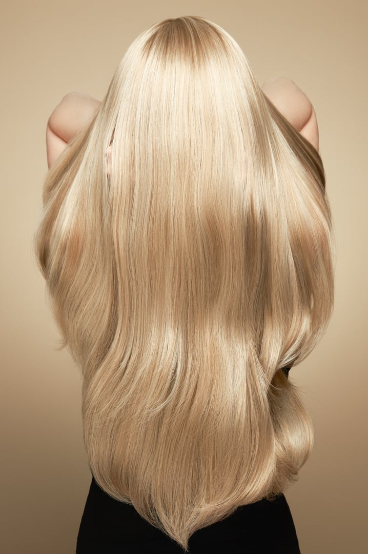 Back view of woman with long beautiful blond hair isolated on beige background. Dyeing and hair care. Shiny smooth blonde hair