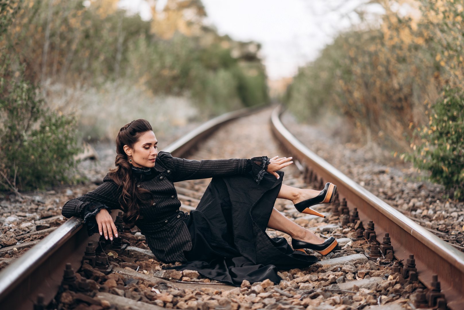 A woman in vintage clothing lies gracefully on railroad tracks against the backdrop of an autumn sunset. The concept of feminism, emancipation, the struggle for equality and independence.