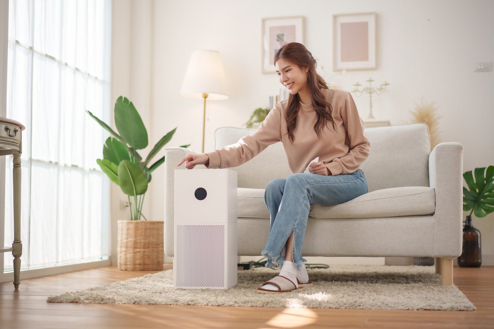 Healthy Asian woman is operating an air purifier while relaxing at home, enjoying a moment of tranquility.
