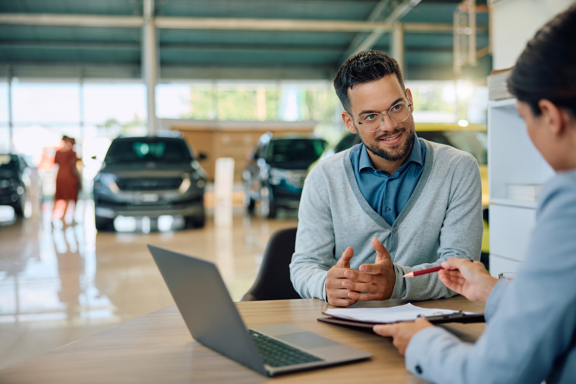 Young man communicating with saleswoman while about to sing a contract for buying new car in showroom.