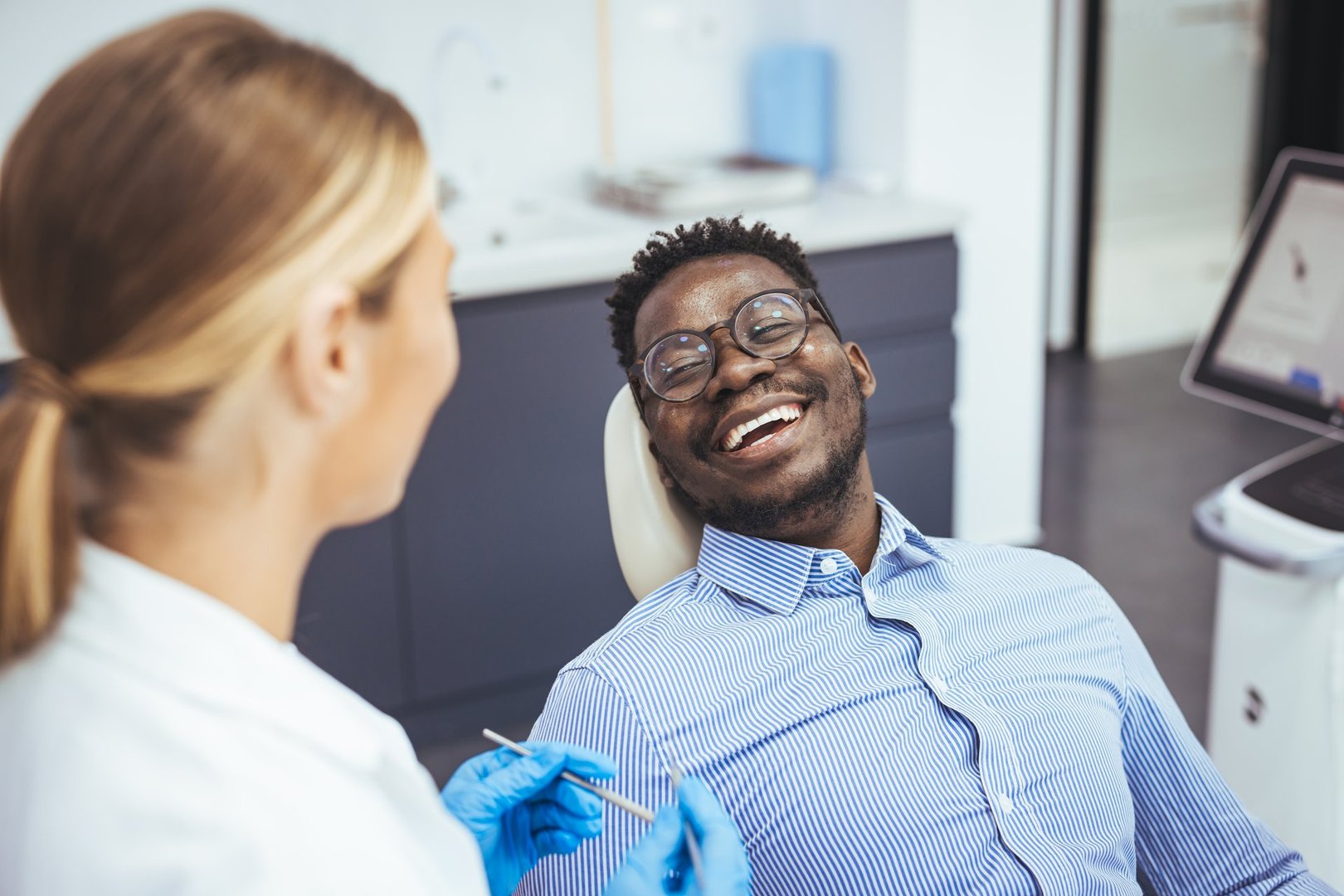 Smiling african guy in dentist chair looking with trust at his doctor, close up. Young African American Man Getting Teeth Treatment With Professional Stomatologist At Modern Clinic