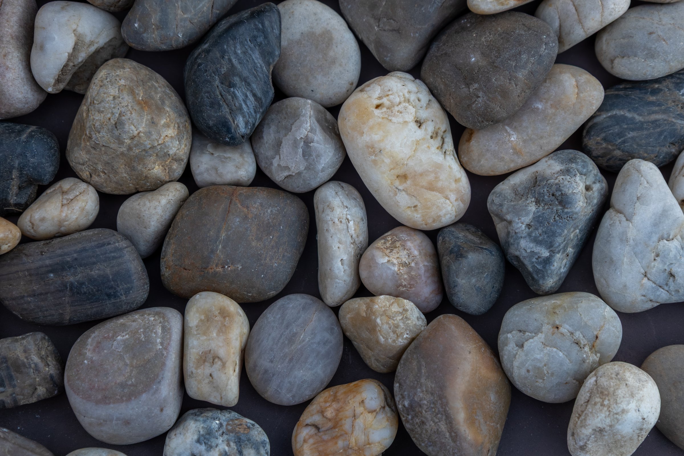 This image shows an abstract texture background of dry river rocks on a dark surface backdrop.
