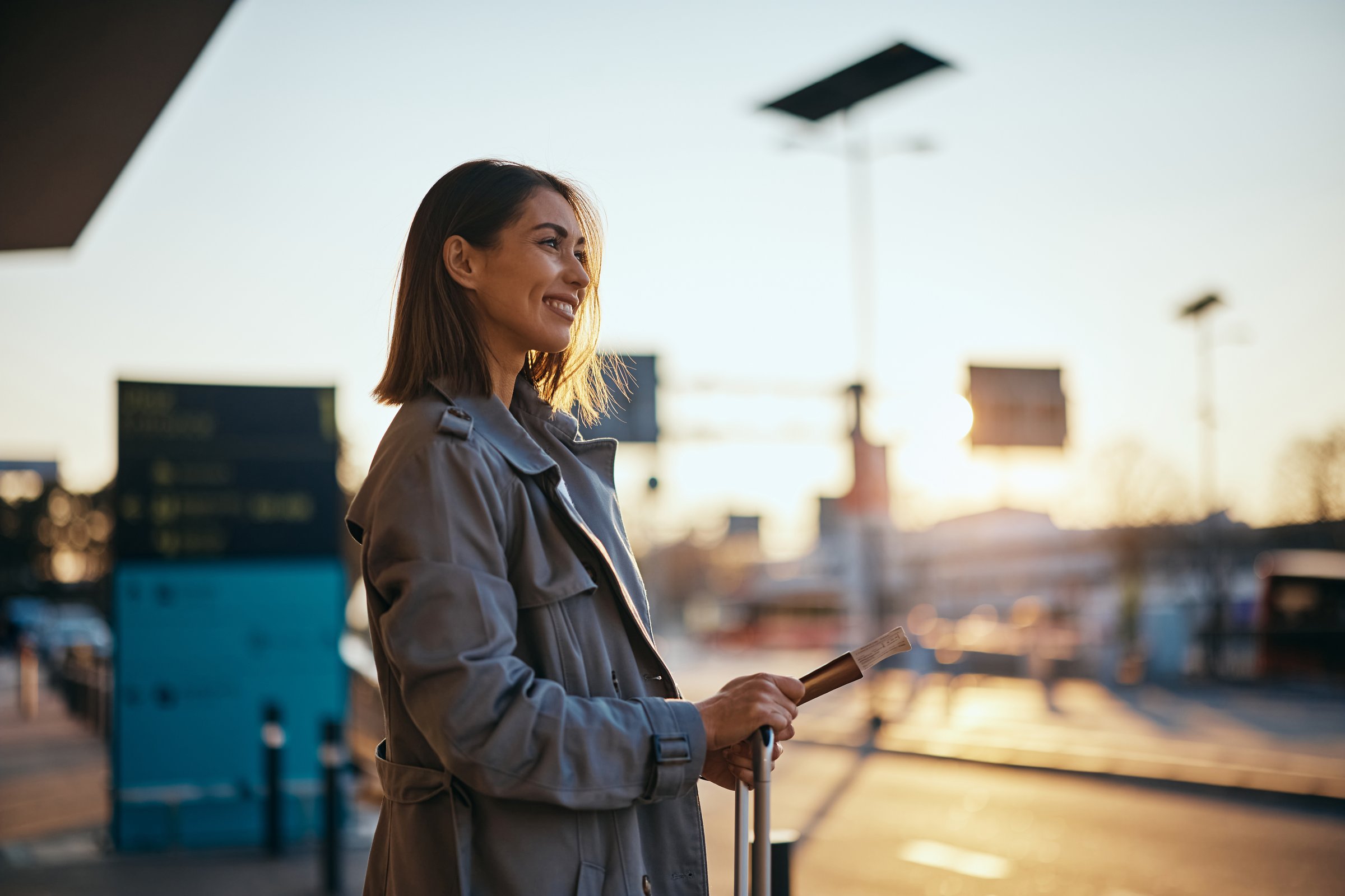 Happy female tourist waiting for a taxi at airport terminal at sunset. Copy space.